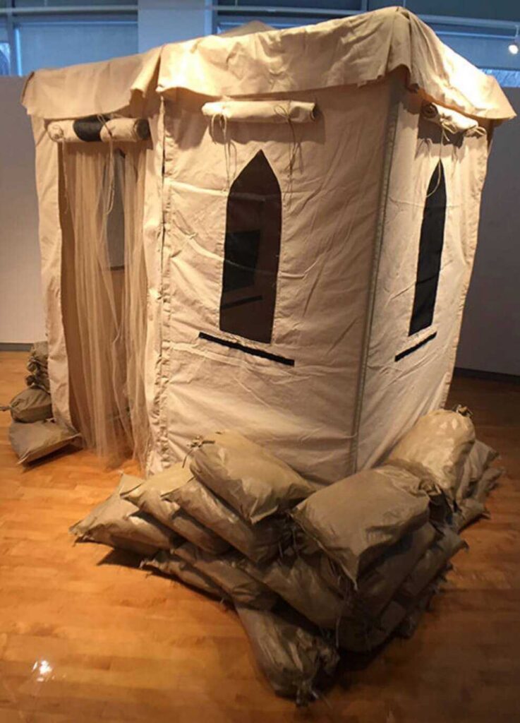 A canvas military style confession booth equipped with sand bags, and mosquito nets