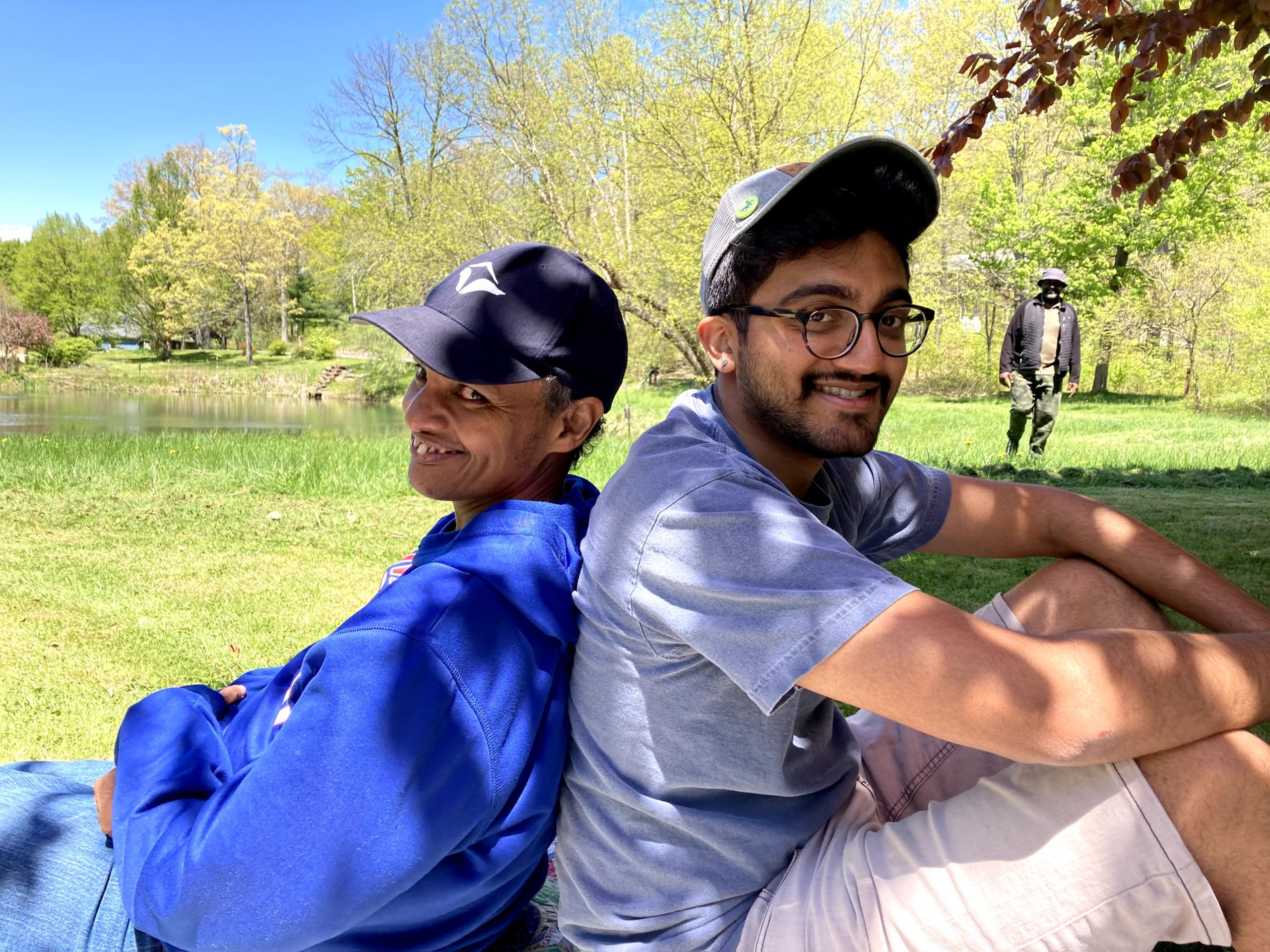 Matt and a friend smile while sitting back-to-back in a field.