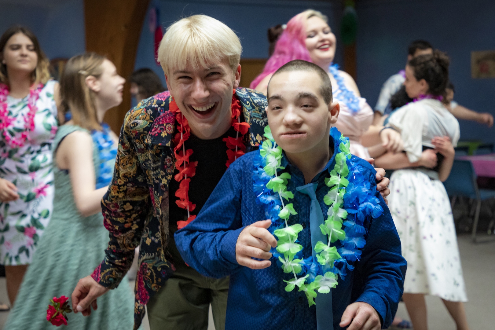 People wearing leis dance with each other and smile for the camera