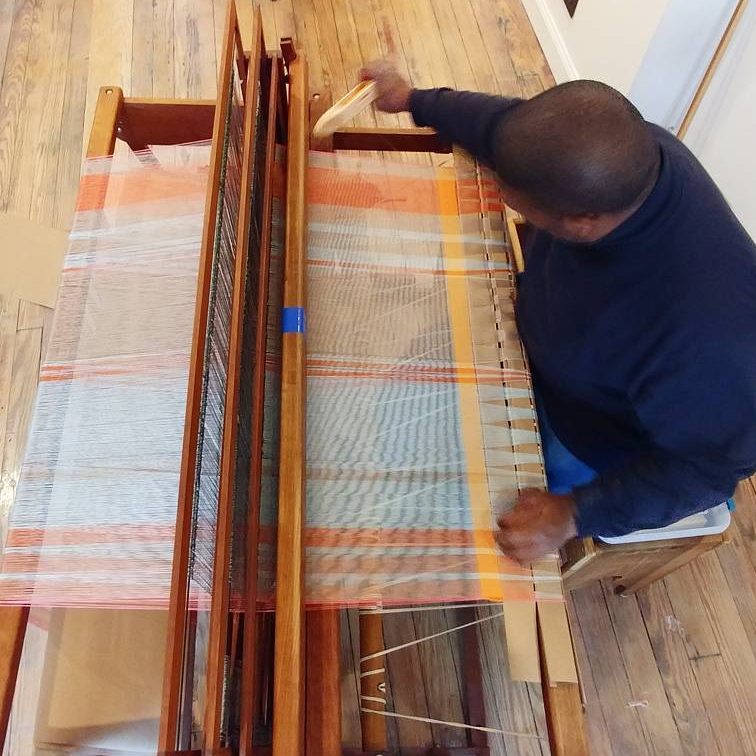 A person weaving cloth on a large floor loom, seen from above.