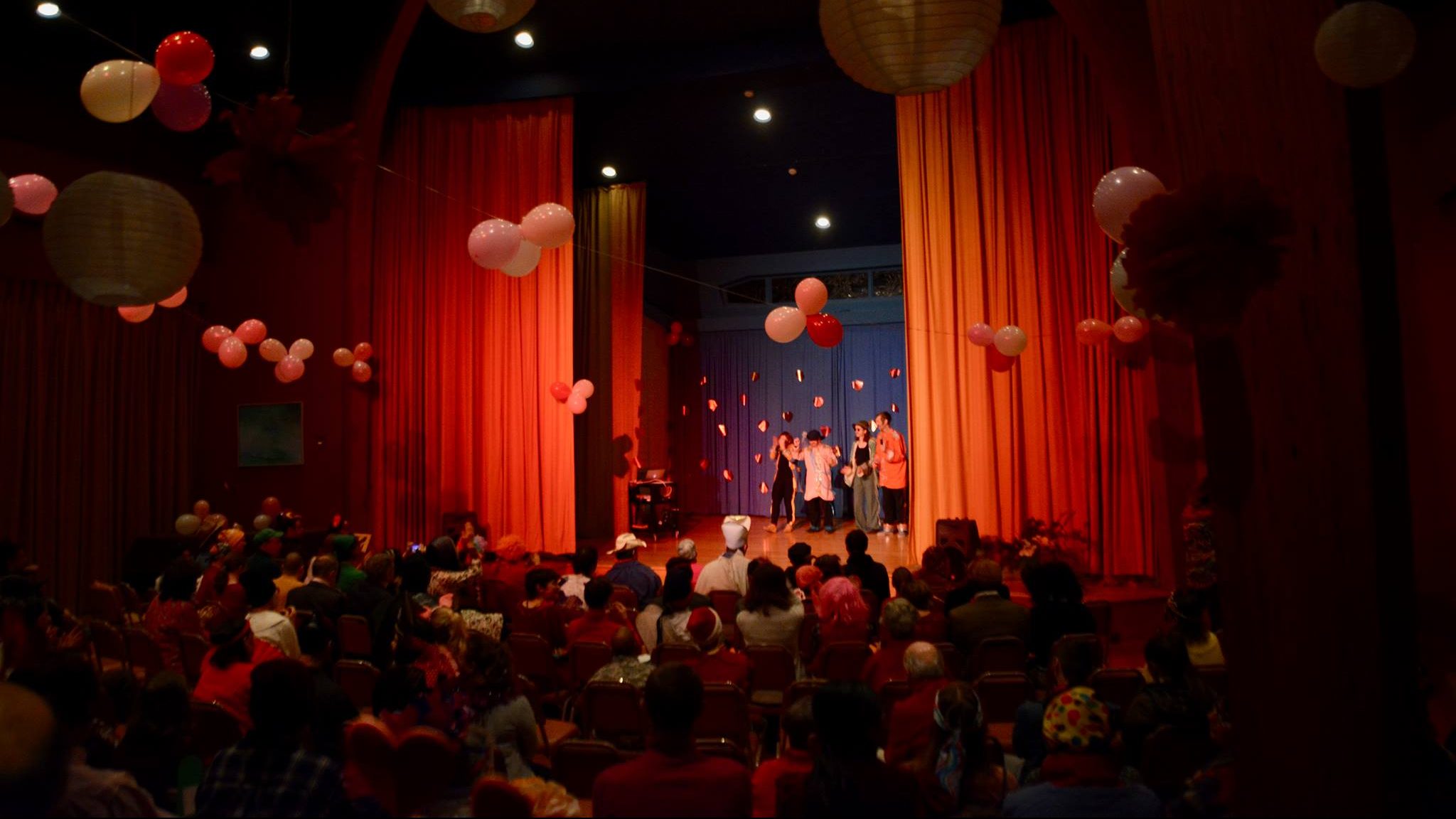 People onstage bow to a full audience as curtains close and confetti falls