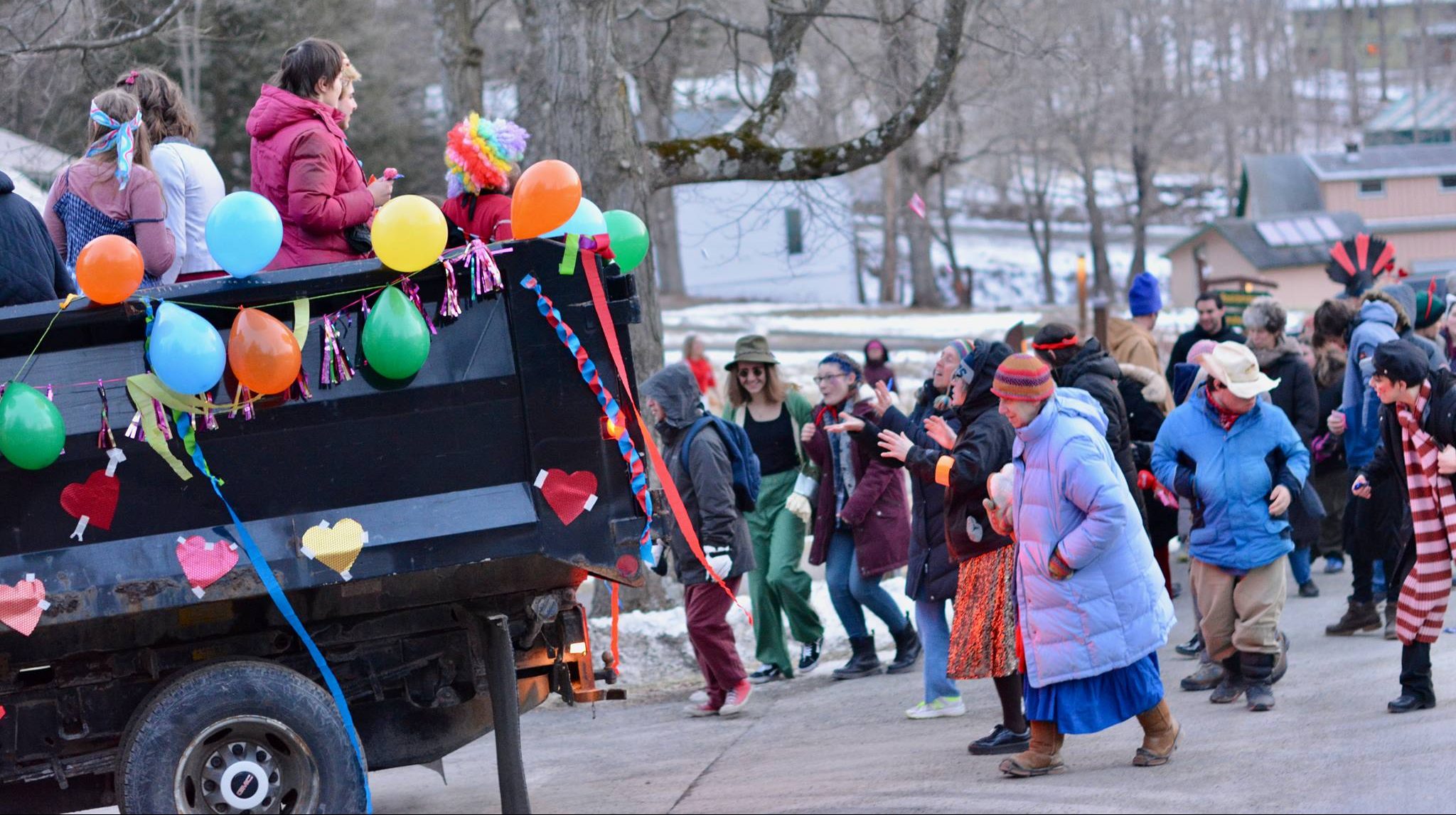 People ride on and follow behind a festively-decorated truck with balloons and paper chains tied to it and cut-out hearts taped to it.