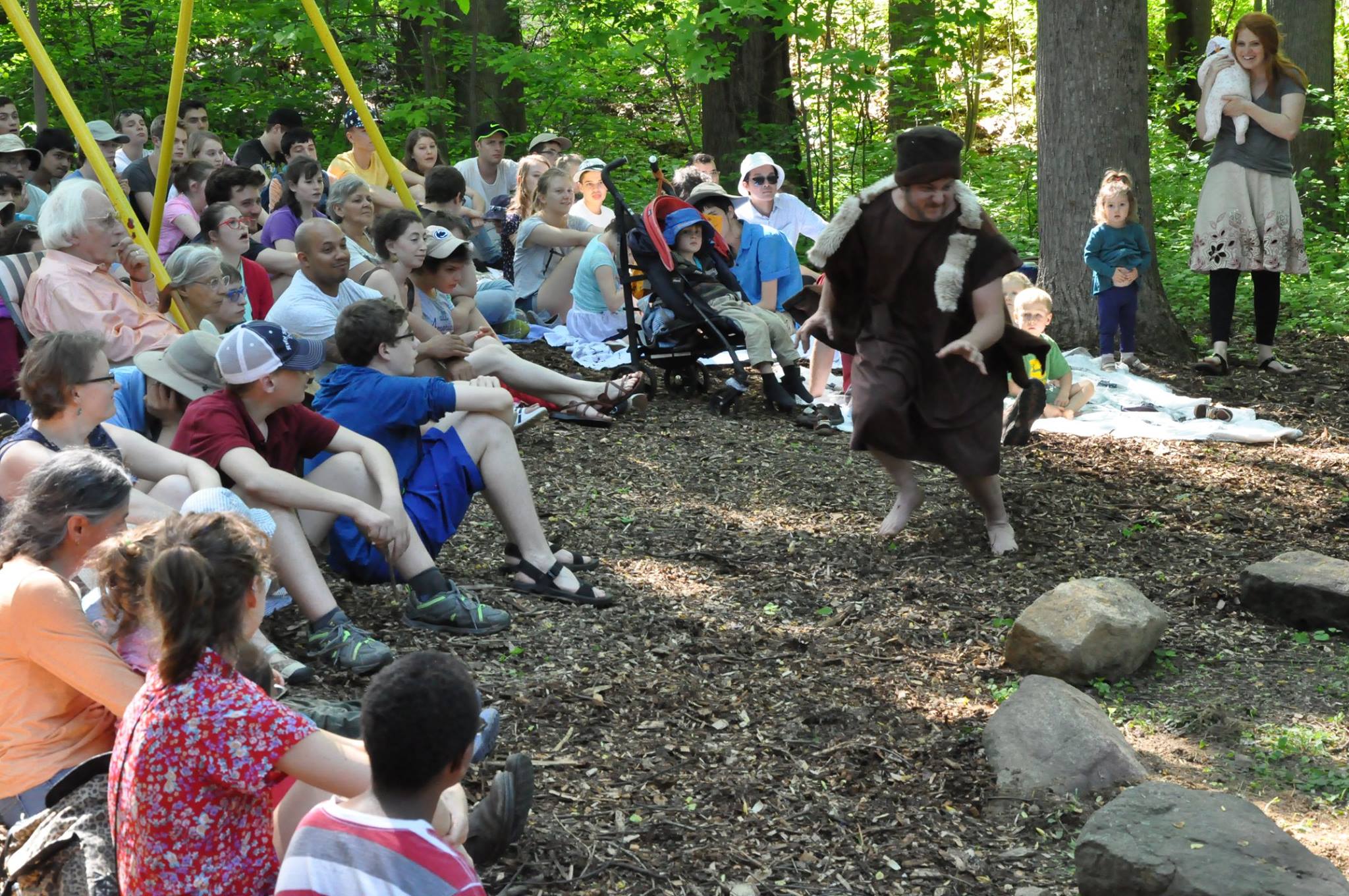People of all ages watch a play being performed in the woods