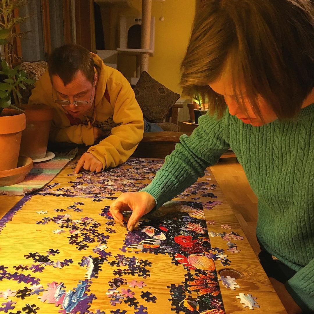 Two people put together a puzzle in a cozy, warmly-lit living room