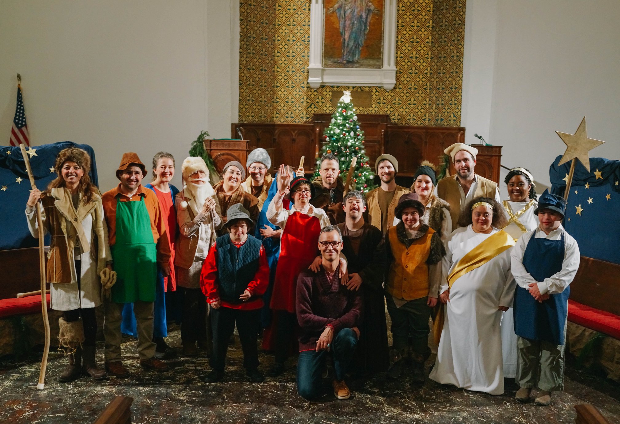 A group of people in and out of costume pose together indoors in front of a Christmas tree.