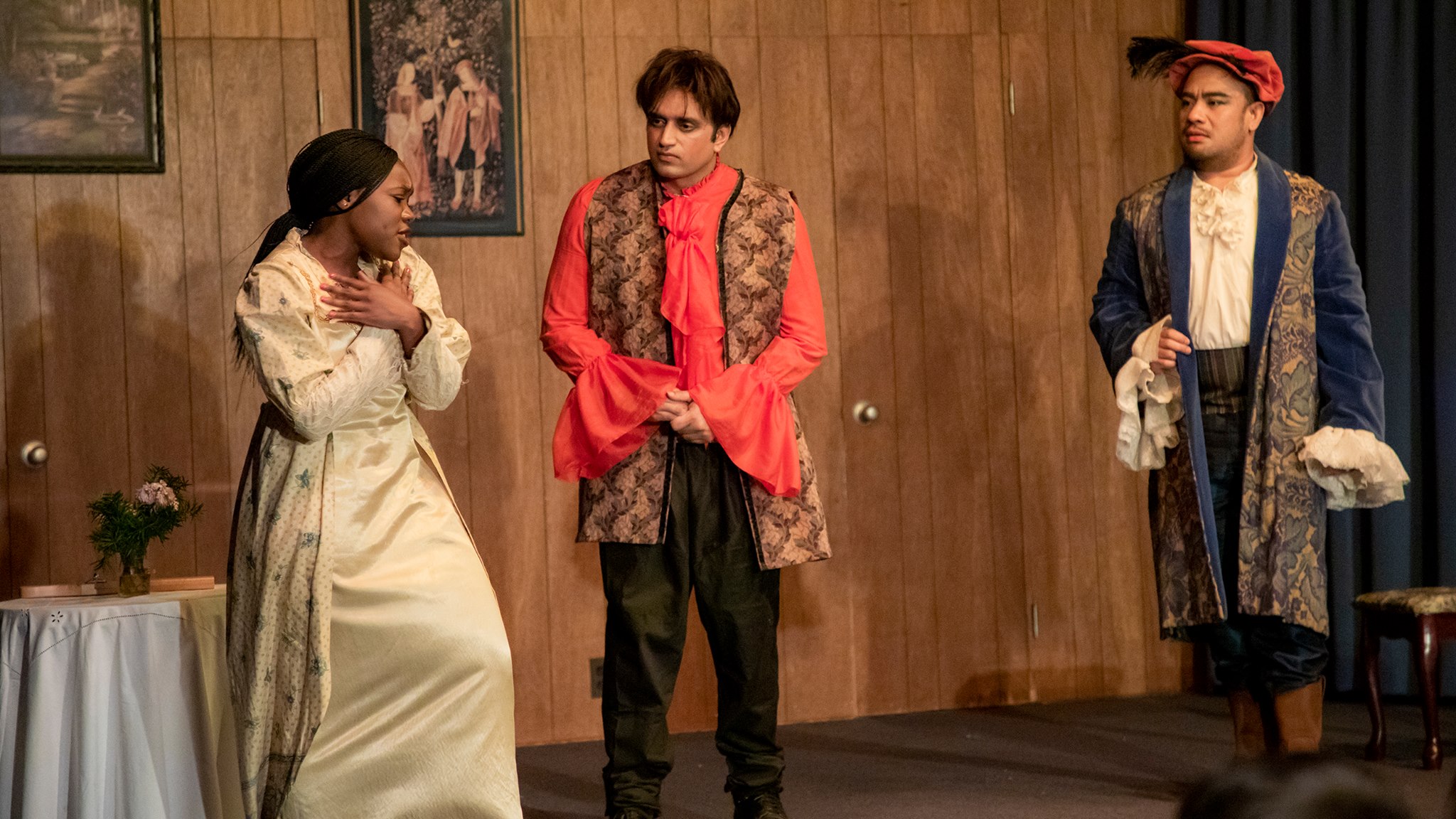 Three people in Shakespearean costume: two young men listen as a young woman expresses distress.
