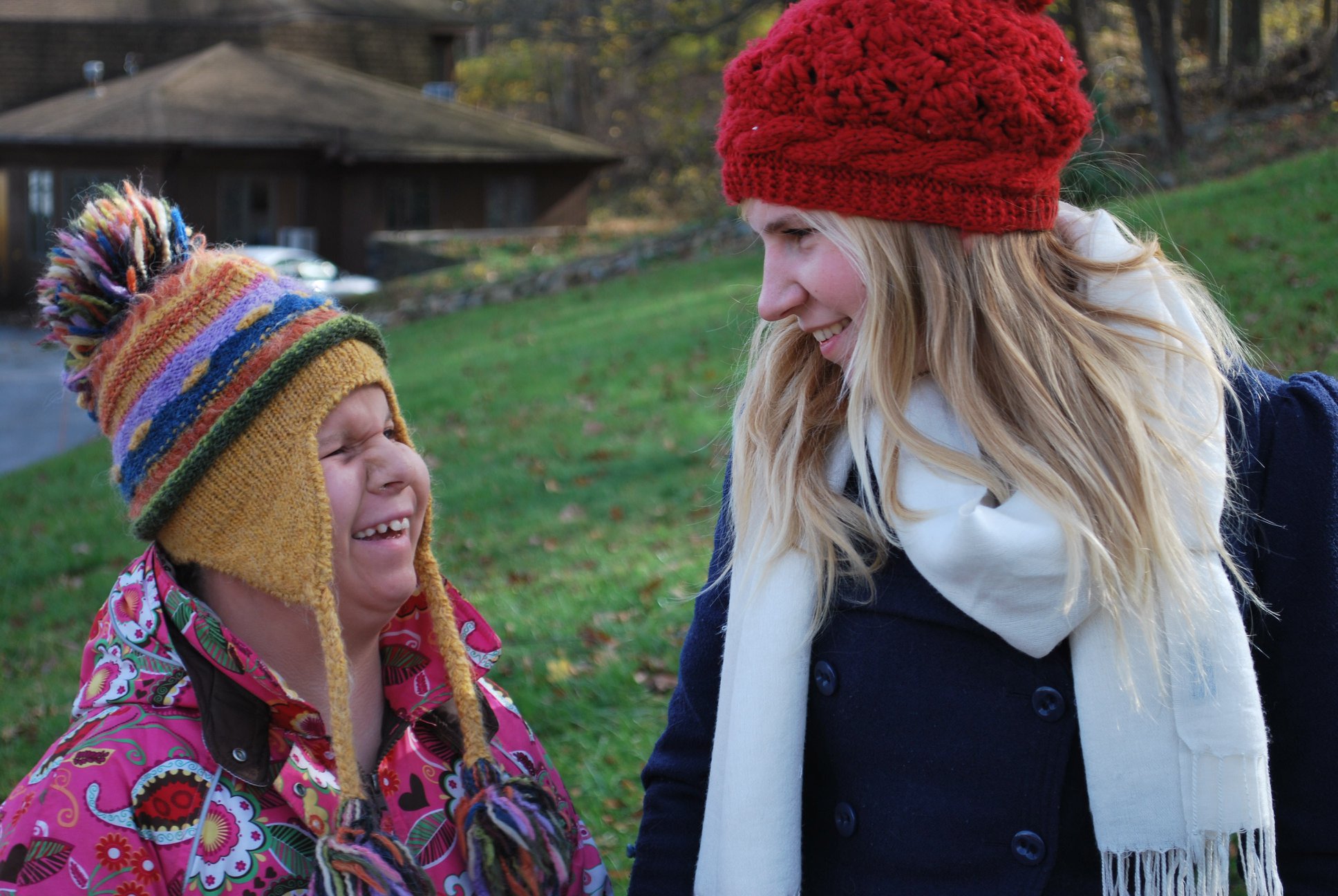 Two people in cozy knit hats, smiling at each other outdoors