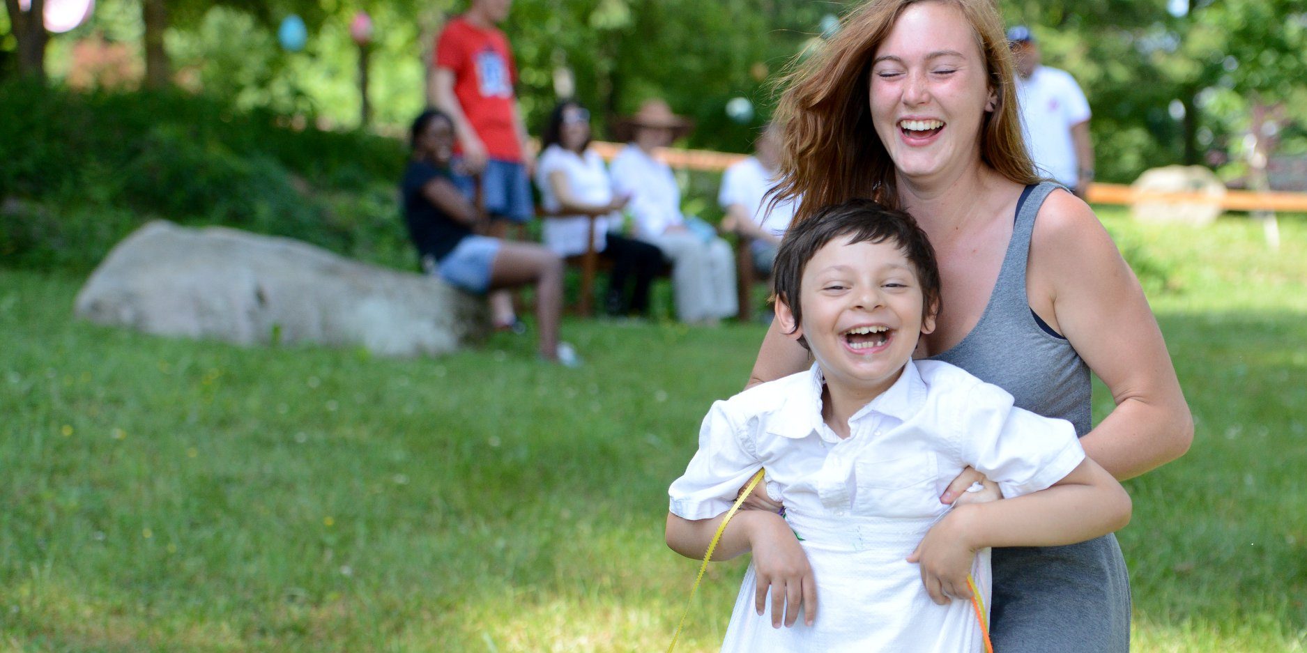 A young woman and a little boy laugh together as she helps him up