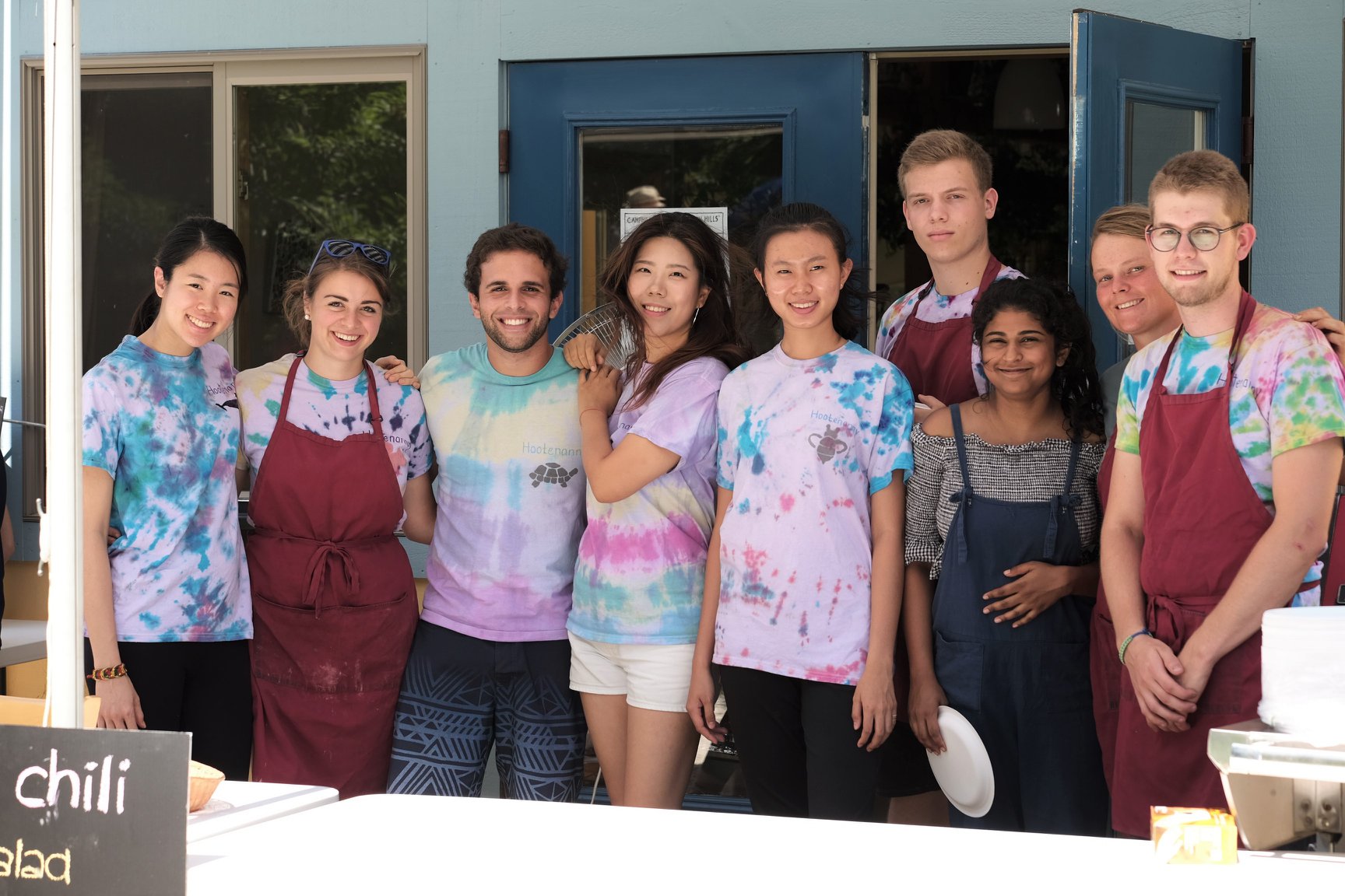 A group of people in aprons and tie-dye shirts posing together and smiling for the camera.