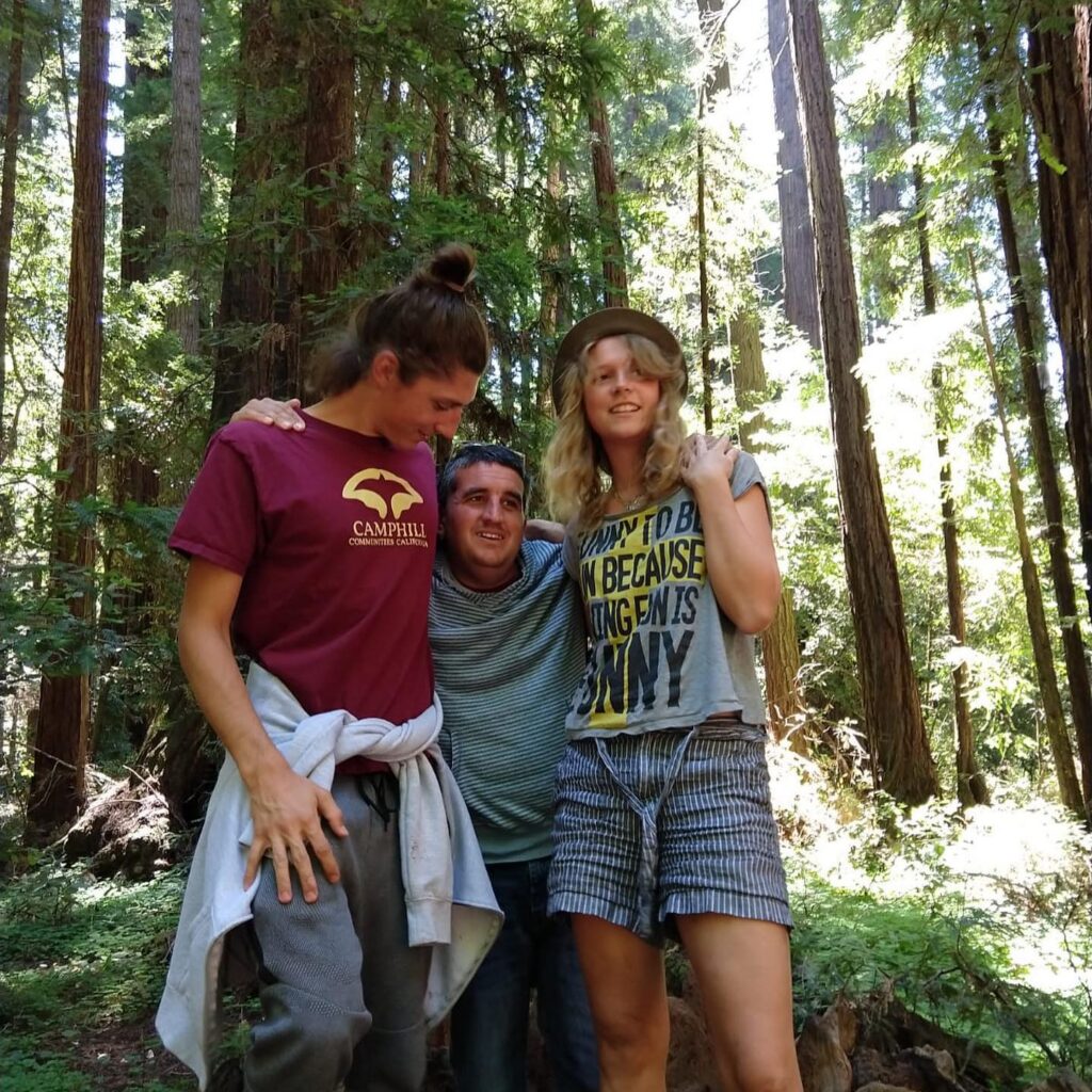 Three people stand together and hug outside in the forest