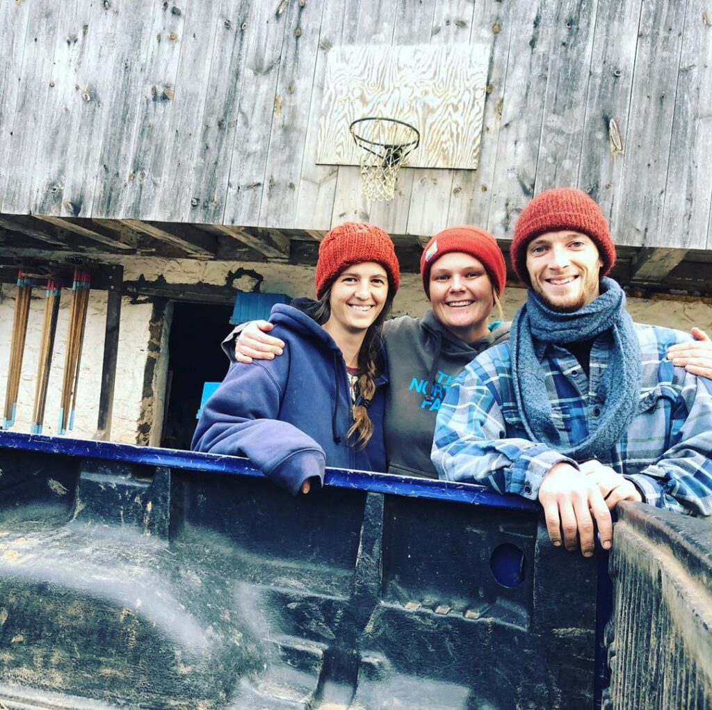 Three people in red knit hats pose together next to the bed of a truck.