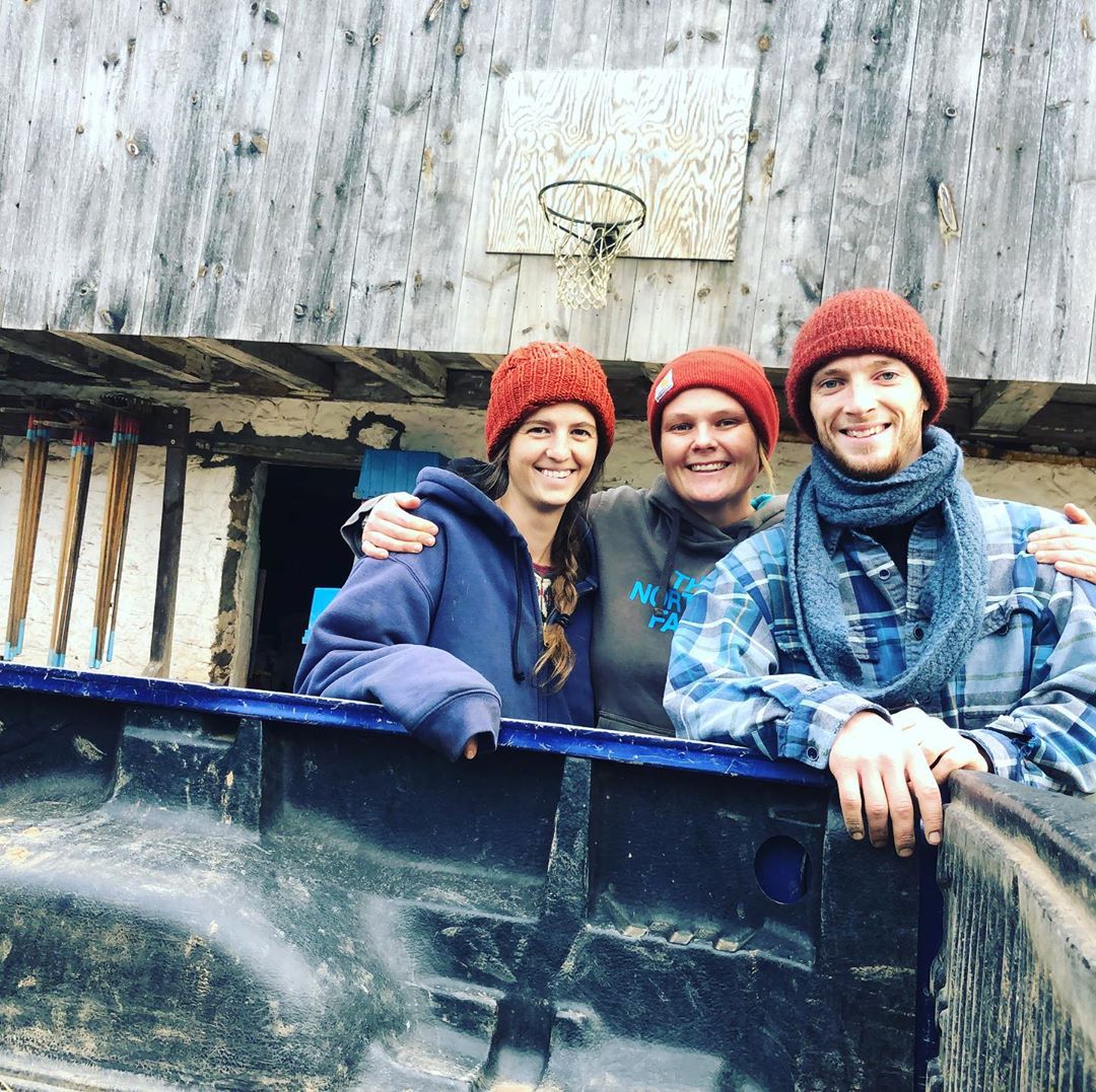 Three people in red knit hats pose together next to the bed of a truck.