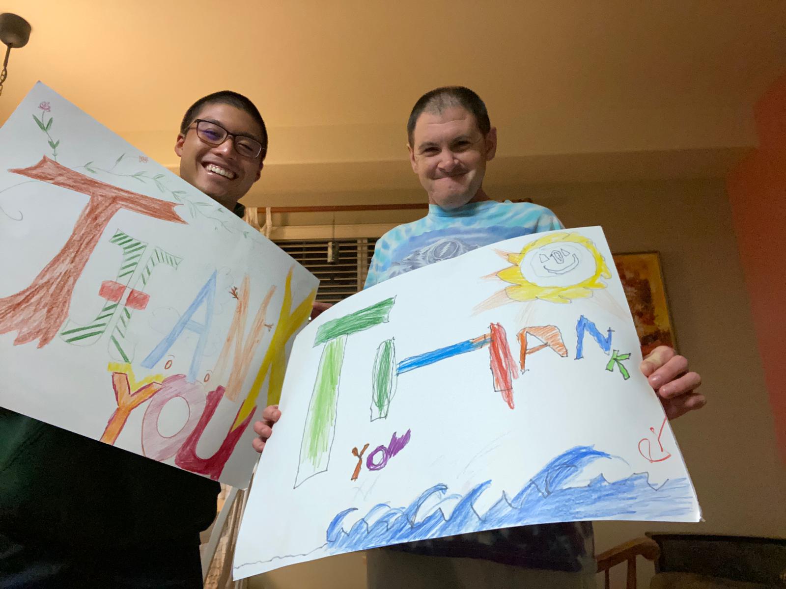Two Camphill residents hold up colorful signs that read "Thank you"