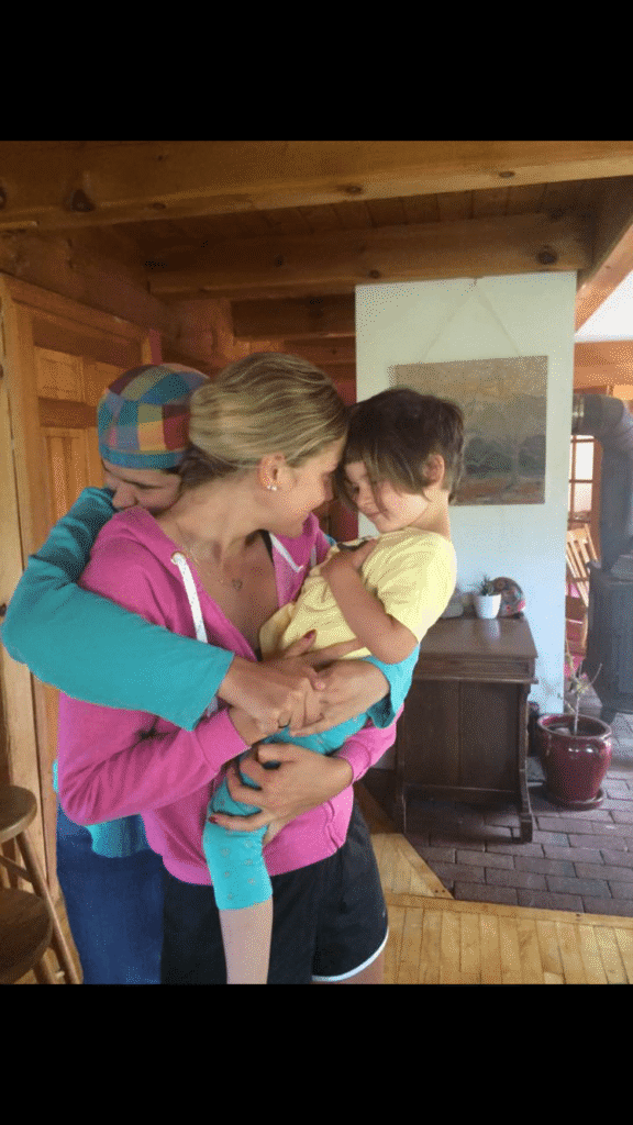 Anna holding a toddler while they smile at each other. A second adult hugs the two of them.