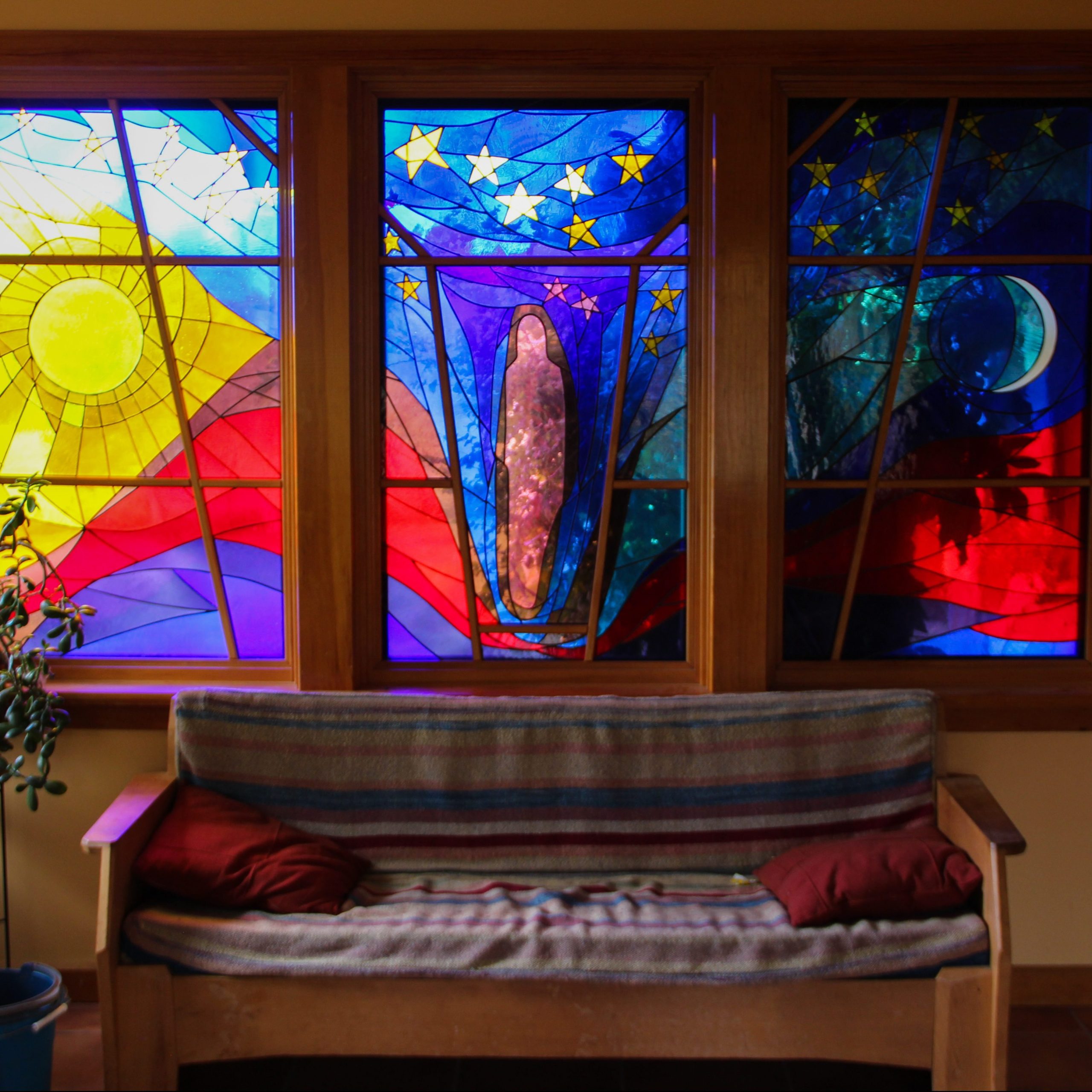 A stained-glass window with a bench couch in front of it.
