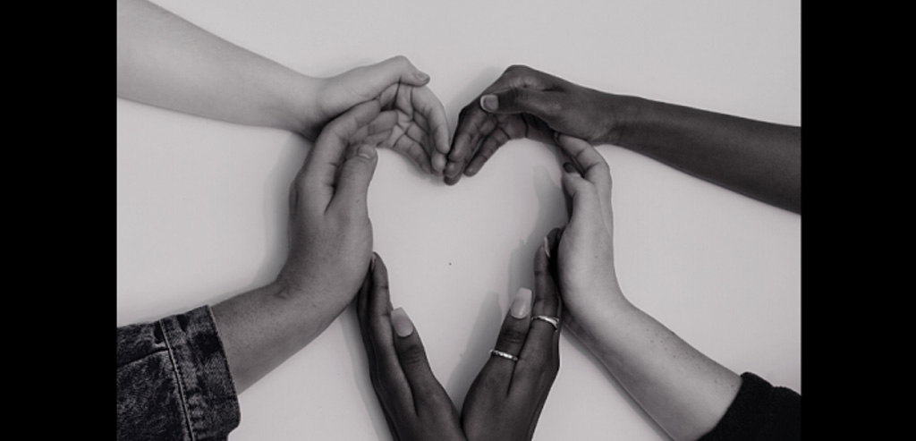 A black-and-white photo of hands of different skin colors making a heart together