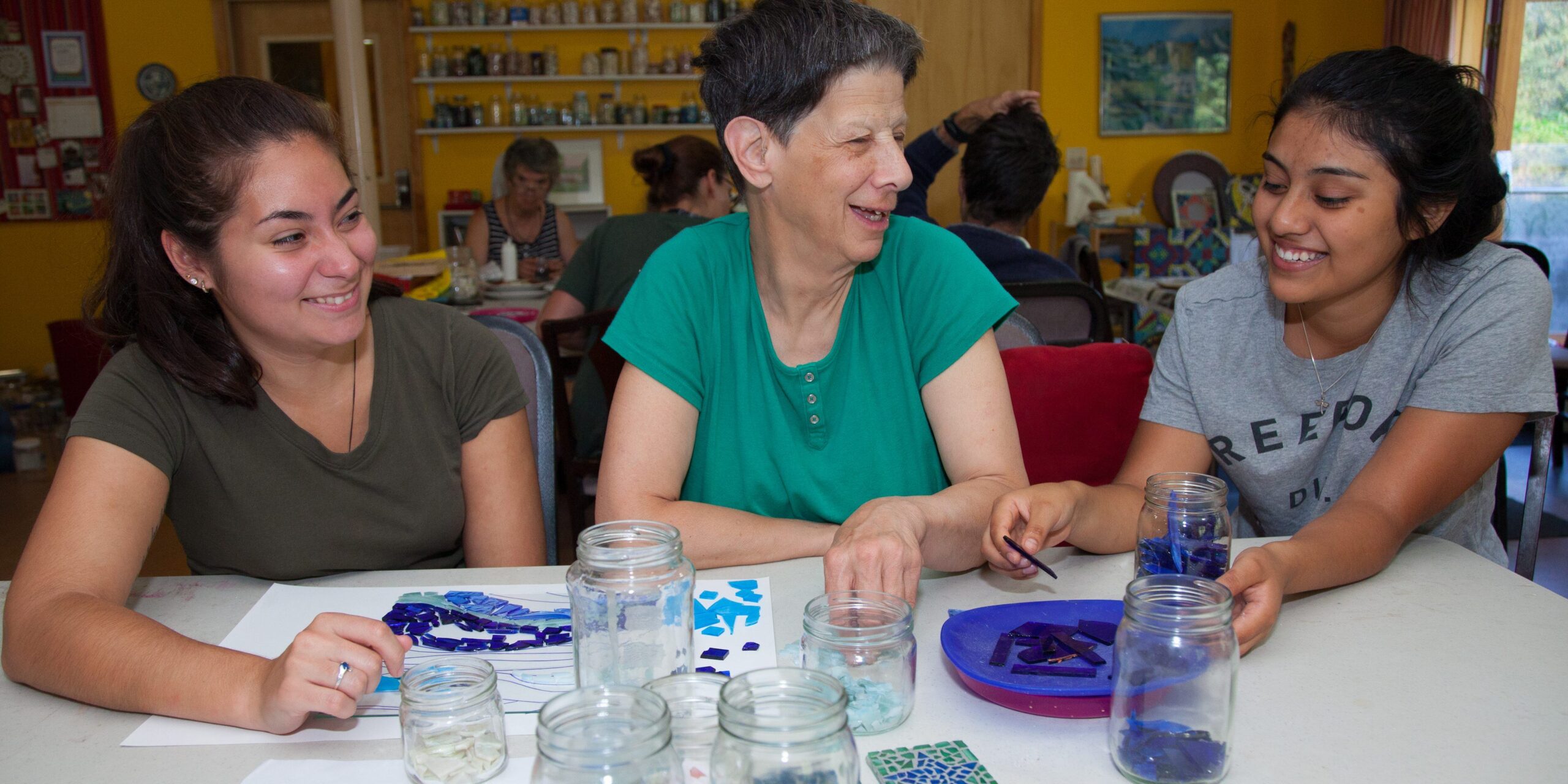 Three people work together on a mosaic of blue tiles.