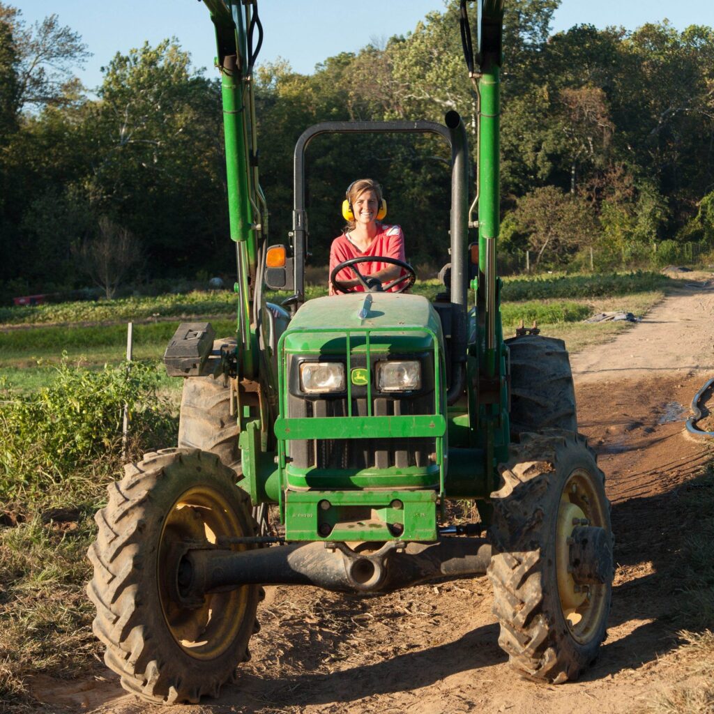 A woman wearing ear protection drives a large green tractor