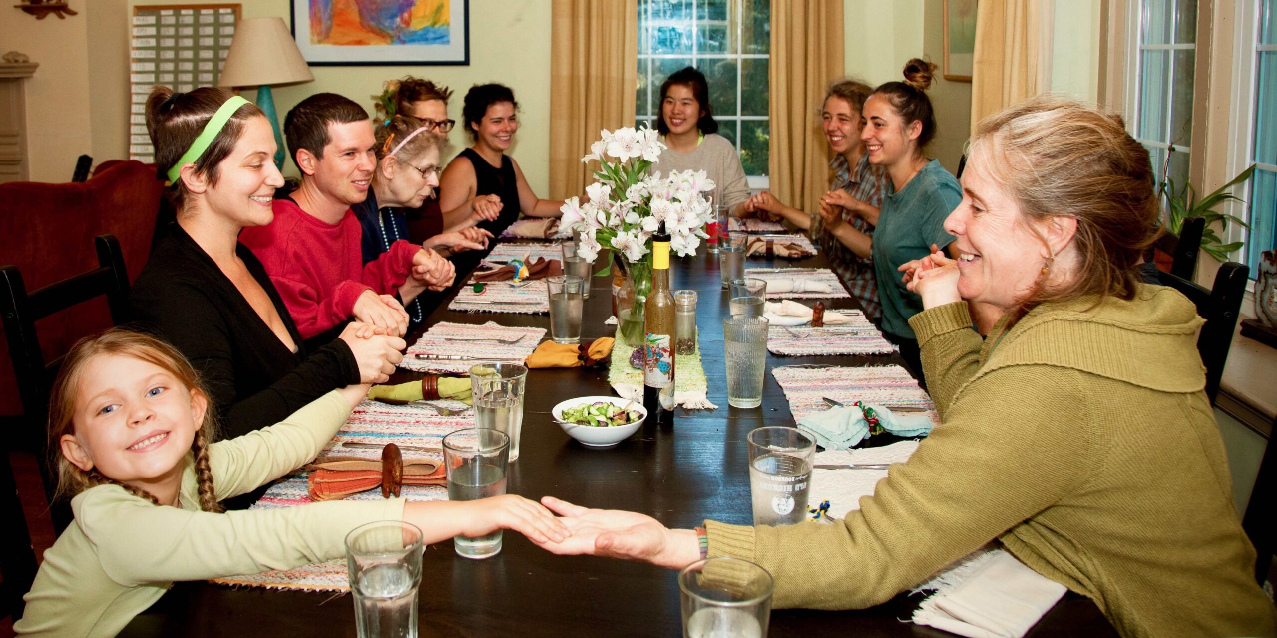 Ten people of all ages hold hands around a table