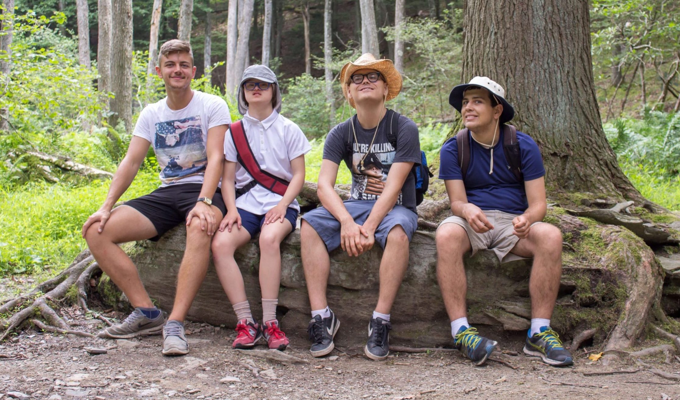 Four people in hiking clothes sit together on a large rock in the woods.