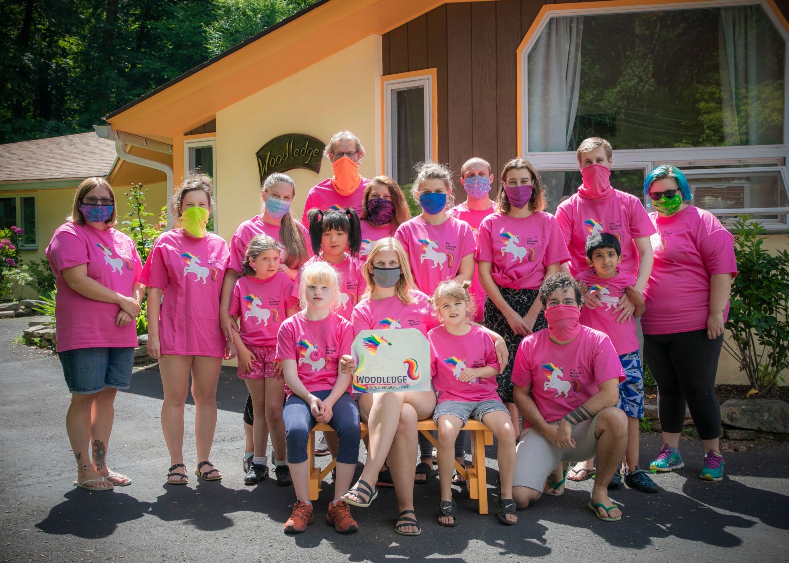 People in cloth face masks and hot pink shirts with unicorns on them, posing together in front of Woodledge House.