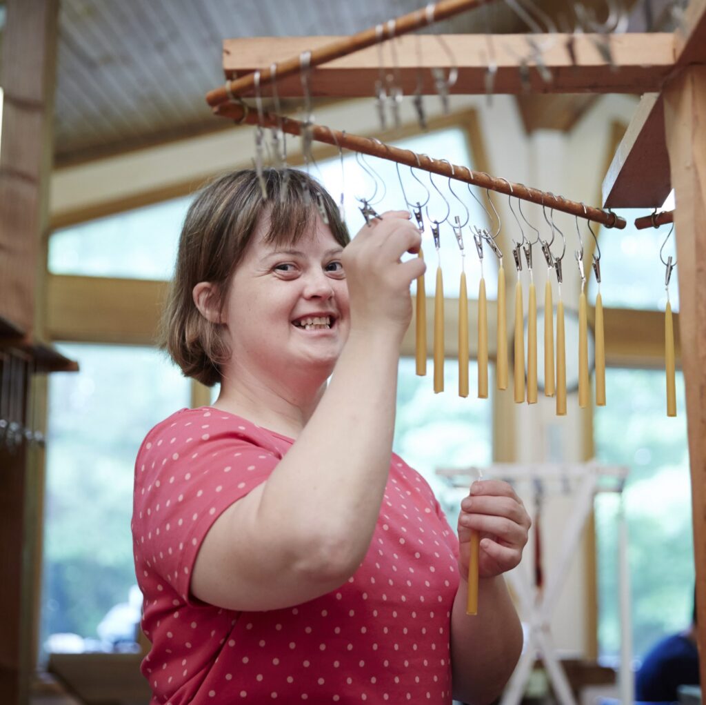 A young woman smiles at the camera as she hangs freshly-dipped candles to dry.