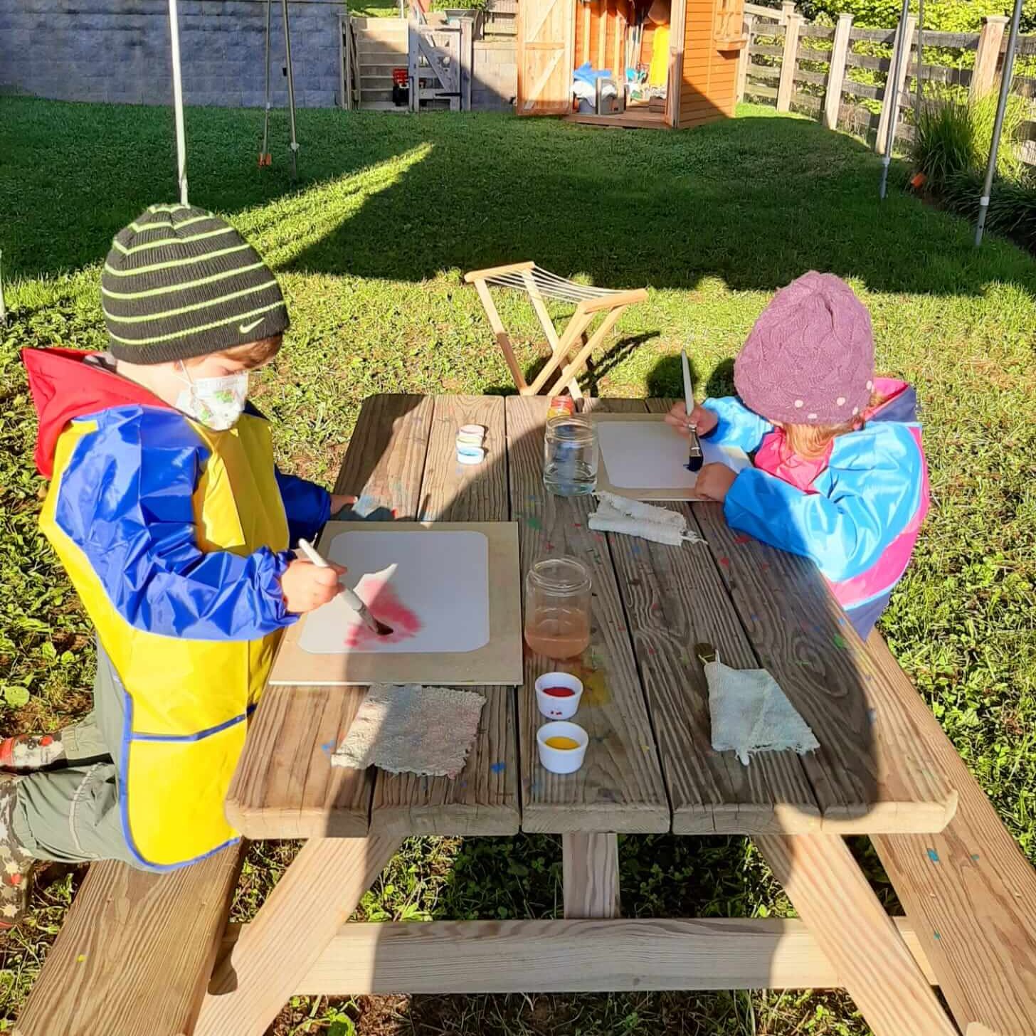 Two Camphill School students watercolor outdoors at a wooden picnic table