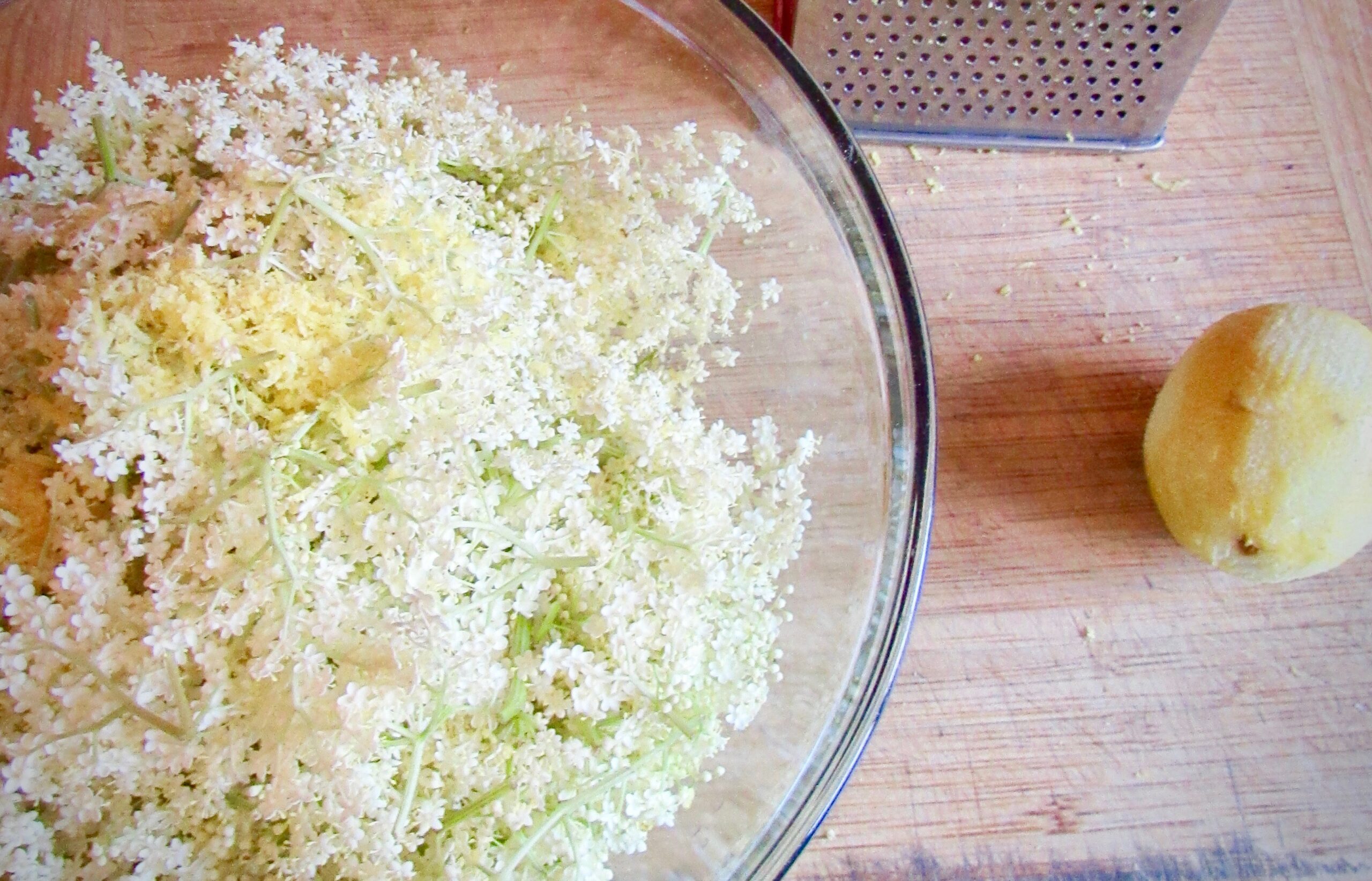 Elderflowers in a bowl on a cutting board next to a grater and a zested lemon