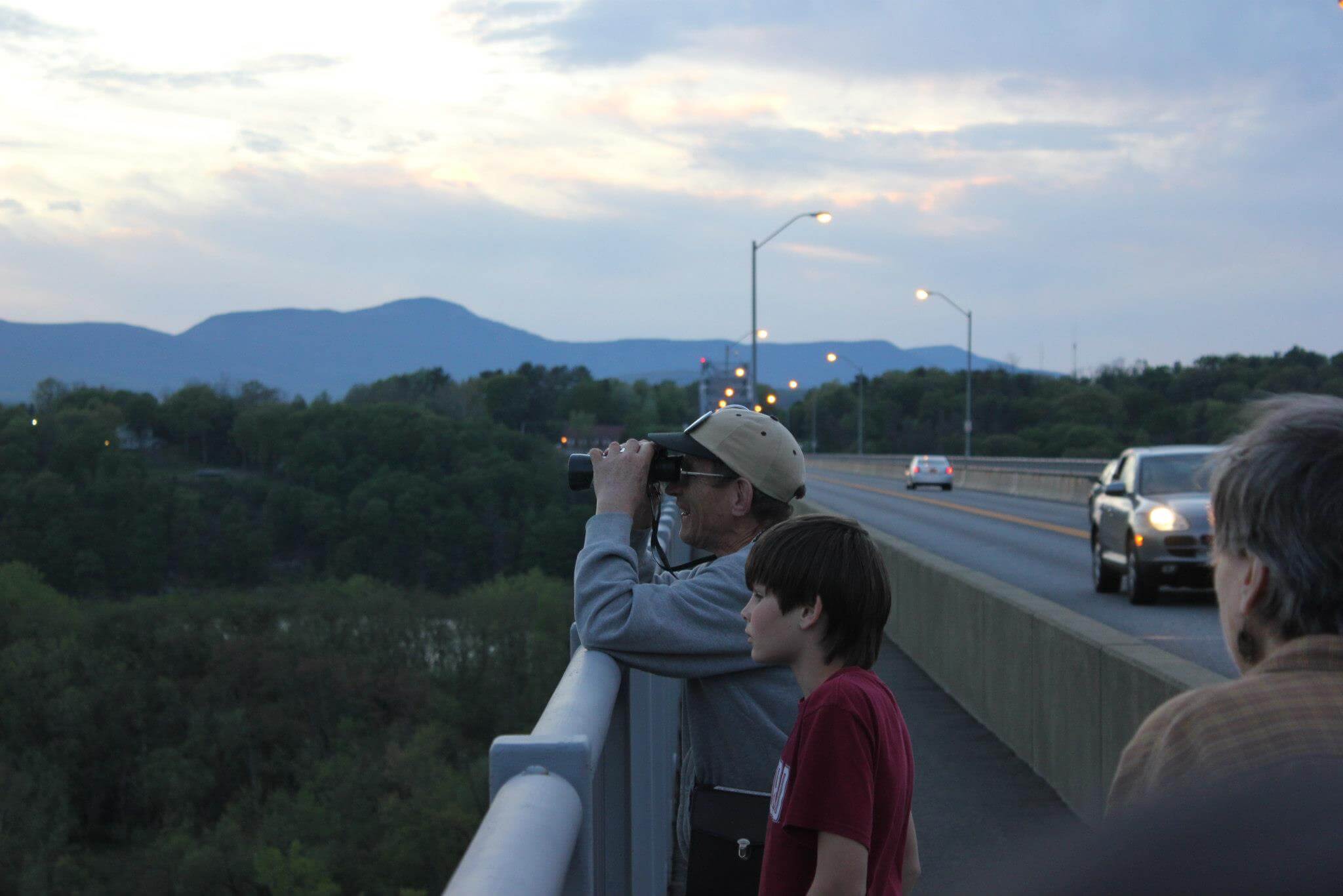 Two people, one young and one older stand next to each other admiring the view off the Rip Van Winkle Bridge. The older man (Elias) has binoculars.