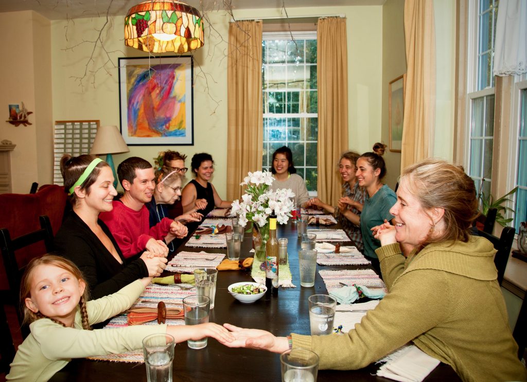 Ten people of all ages hold hands around a table.