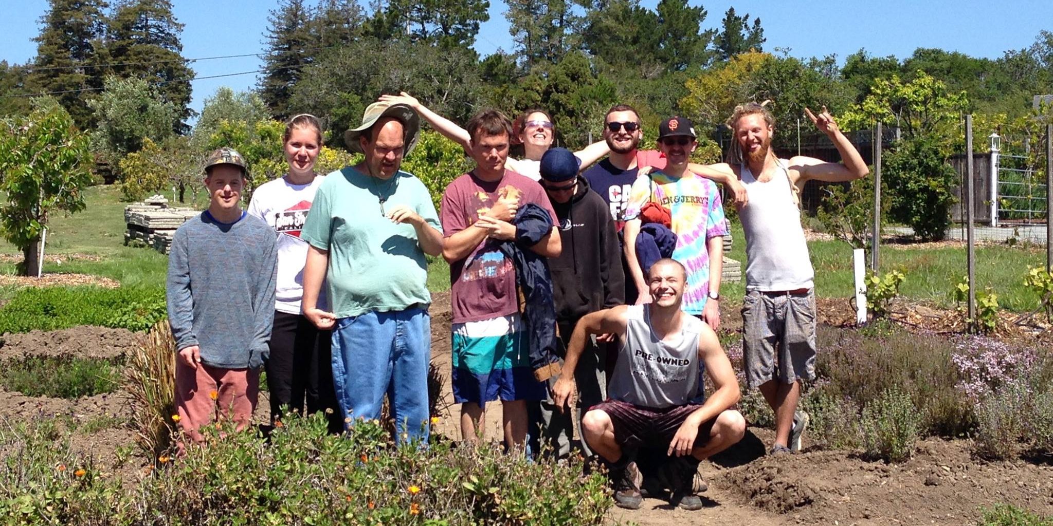 A group of people outdoors in the sunshine in a garden, looking very proud of their work.