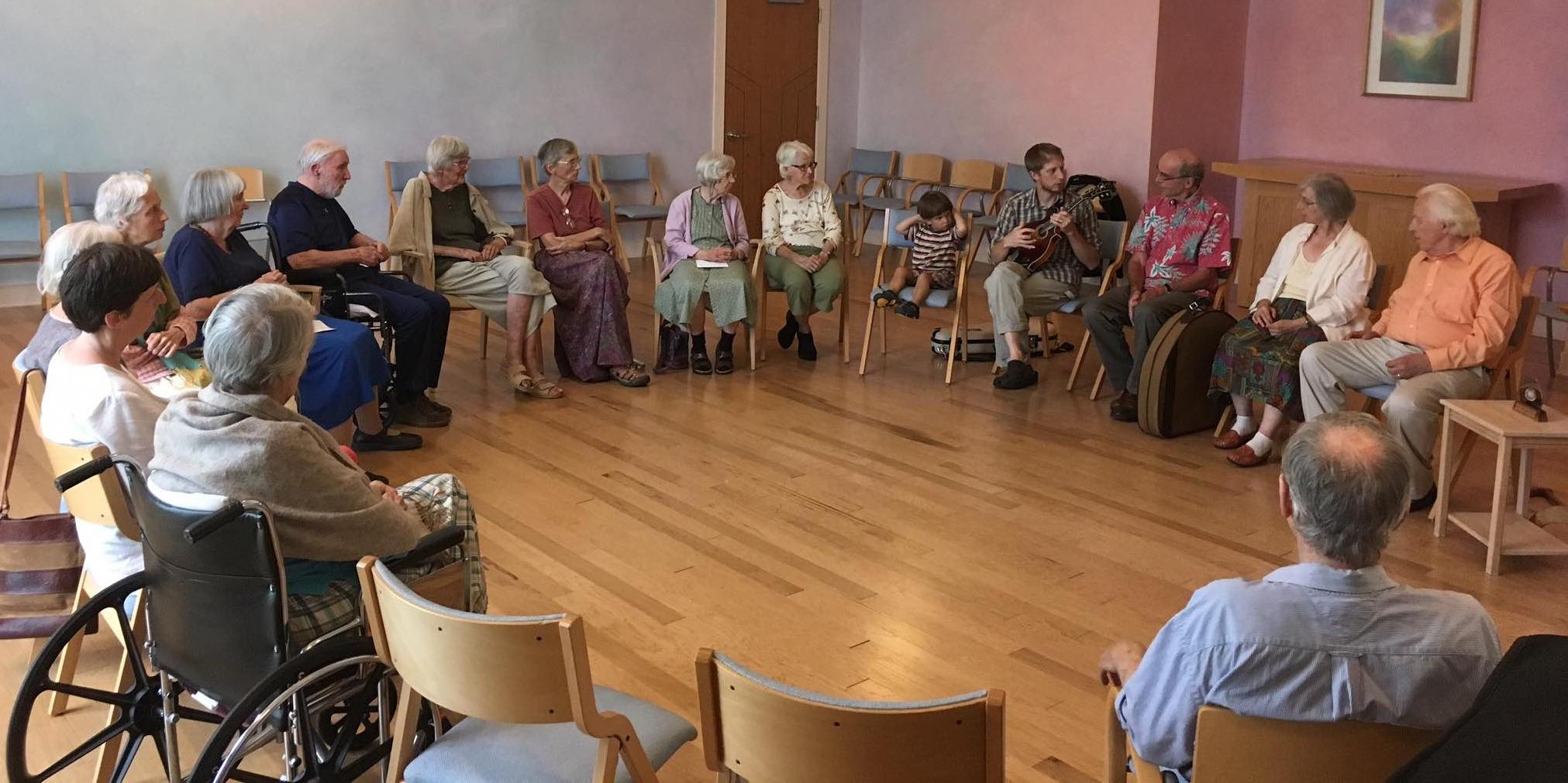 Older adults sit in a circle with a child and a young man with a guitar.