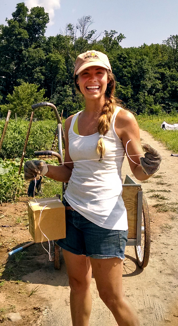 A girl working outdoors holds up a box and a string and smiles at the camera.