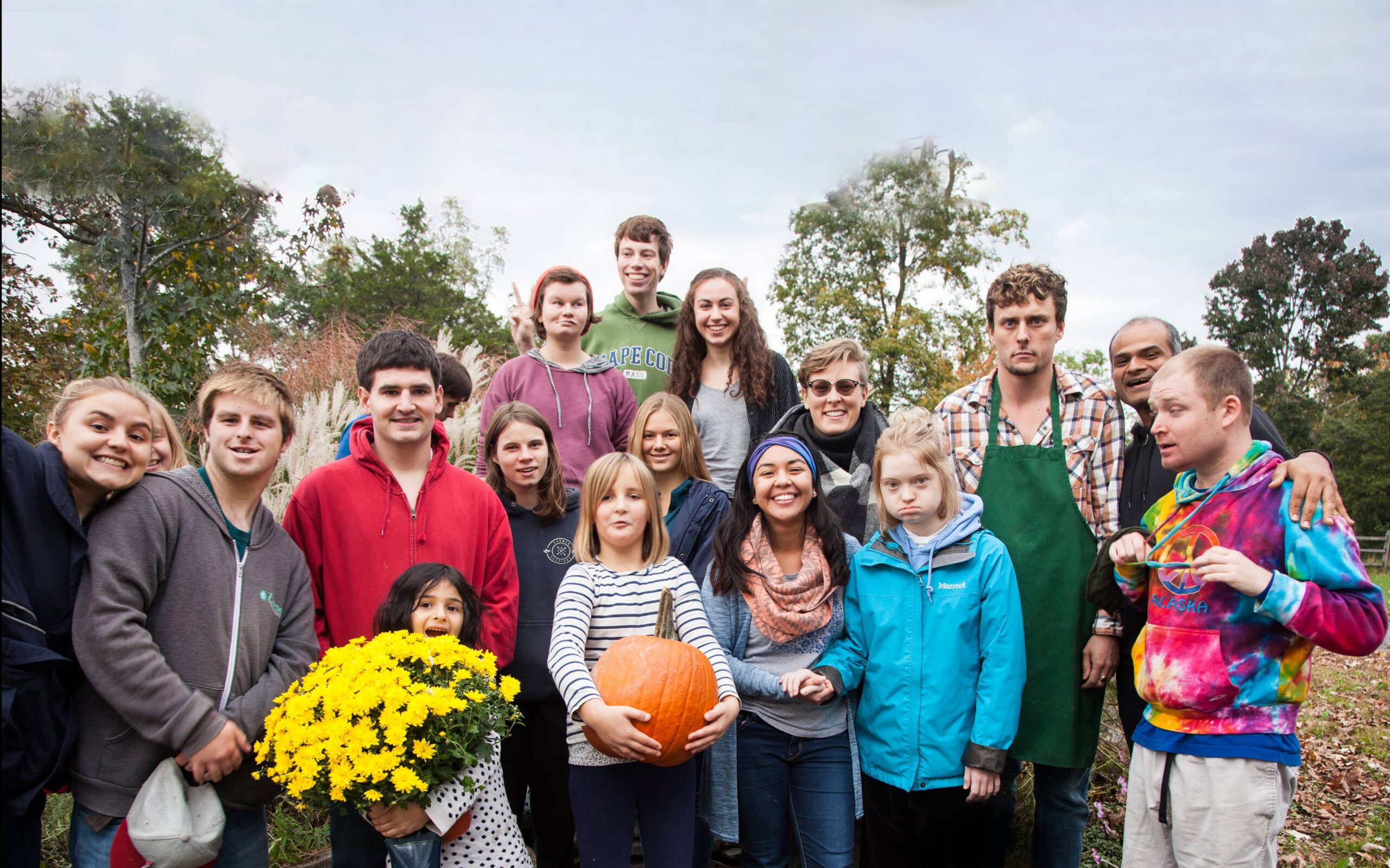A group of children and young adults poses together, holding a pumpkin and a large bouquet of yellow flowers.