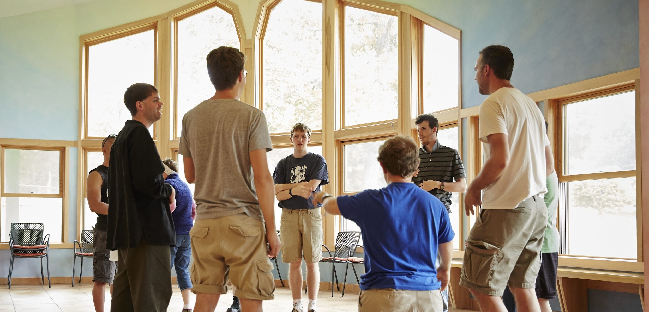People standing in a circle in a room with large windows.