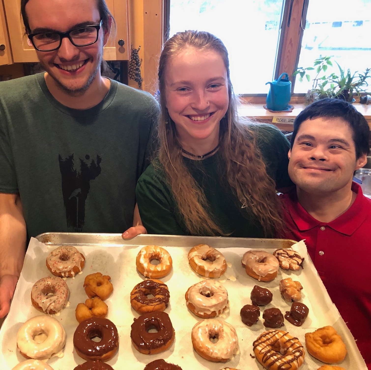 Three people hold up a tray of homemade donuts and smile at the camera