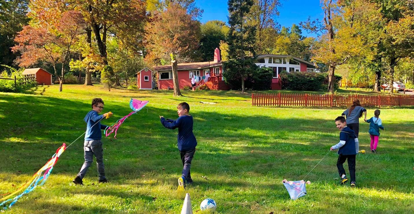 Children flying kites in a wide green field.