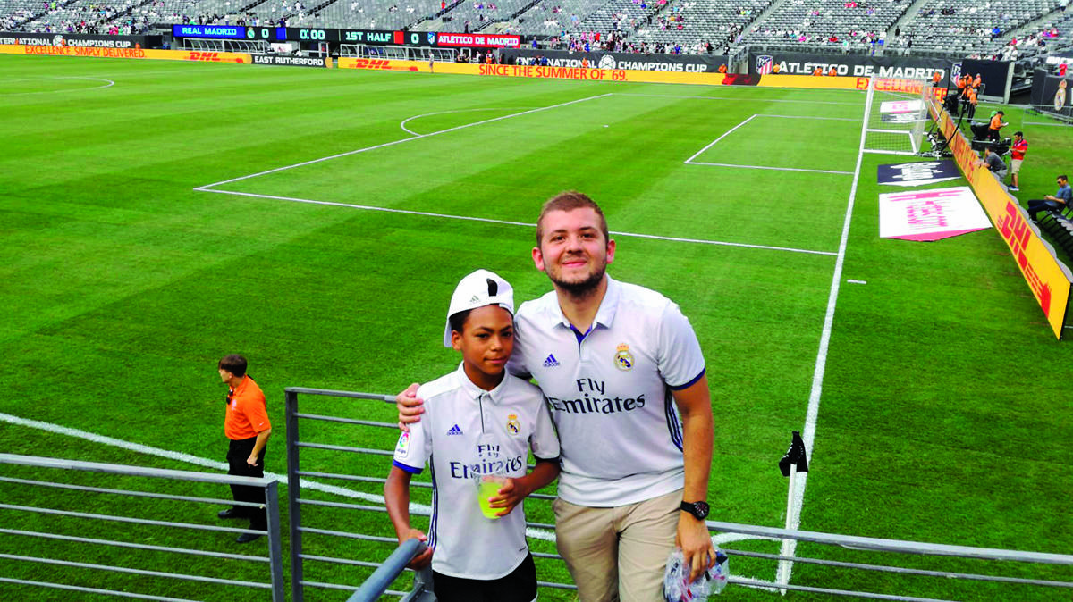 Two people wearing "Fly Emirates" shirts posing in front of a soccer field.