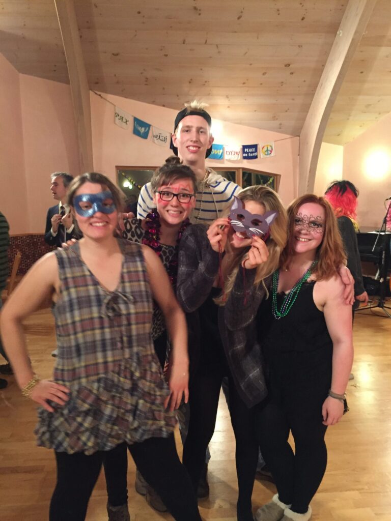 Five smiling people wearing mardi gras masks and necklaces