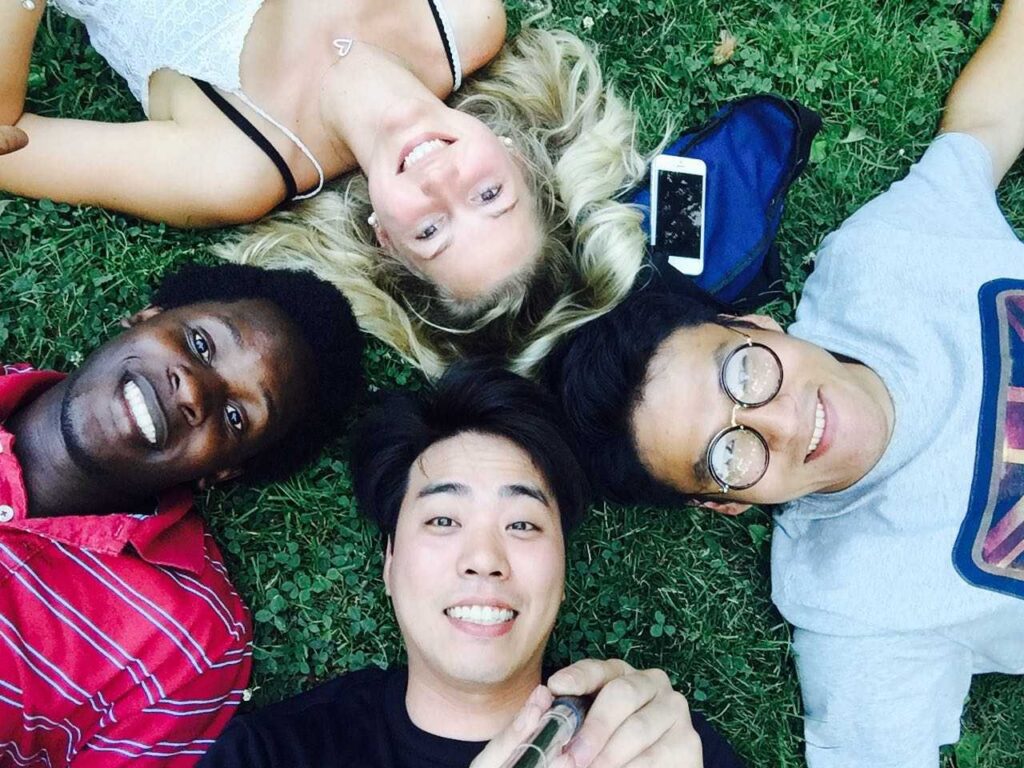 Anna and three friends lying in grass, their heads all together in a circle, looking up