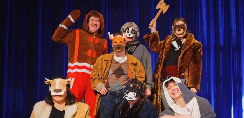 Nicolo is pictured with 6 of his castmates from Jimmy's Journey, smiling in front of a blue curtain. They are all dressed as animals.