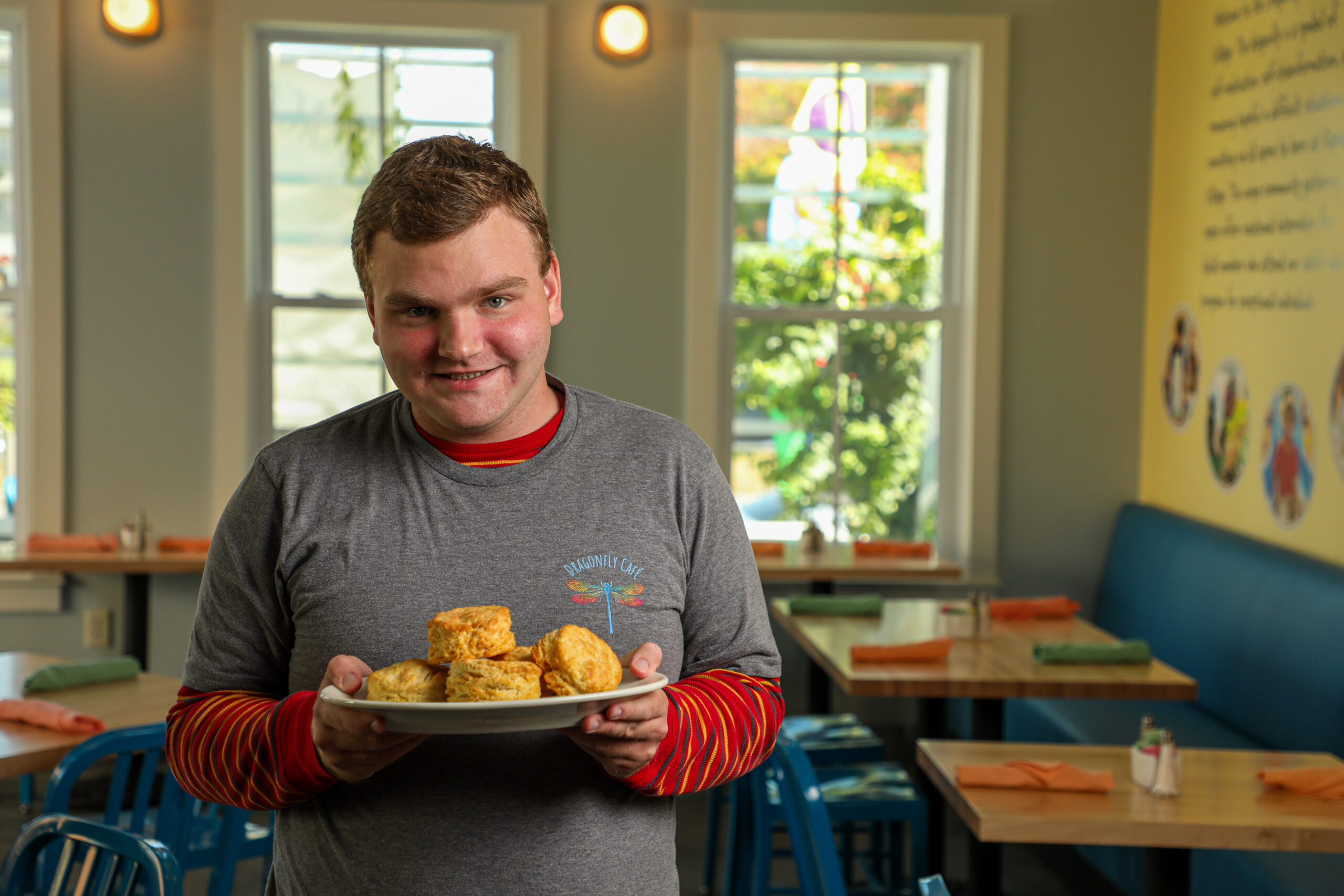 A waiter at Dragonfly Cafe holds a plate of biscuits and smiles at the camera