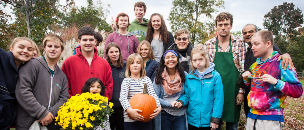 A group of people posing and smiling for the camera, holding a pumpkin and a large bouquet of yellow flowers
