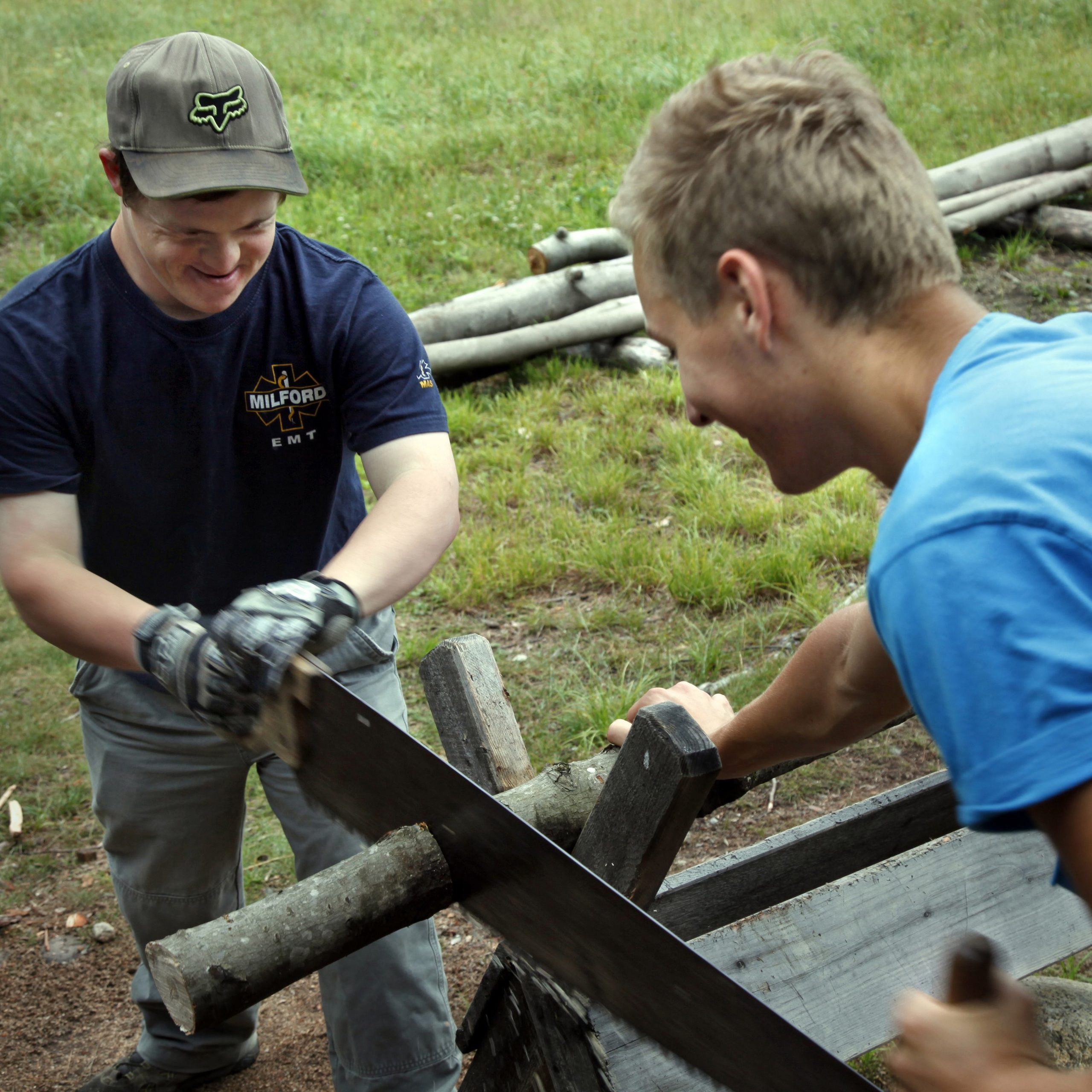 Two boys using a saw to chop up cut trees