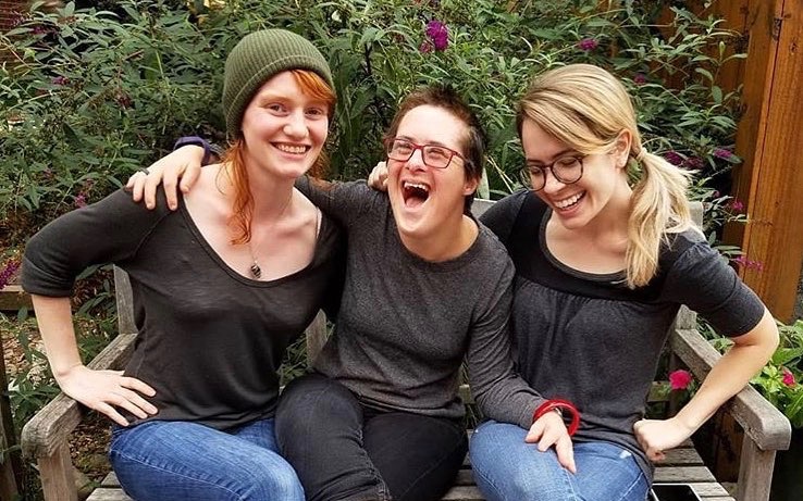 Three women sitting together on a bench and laughing.