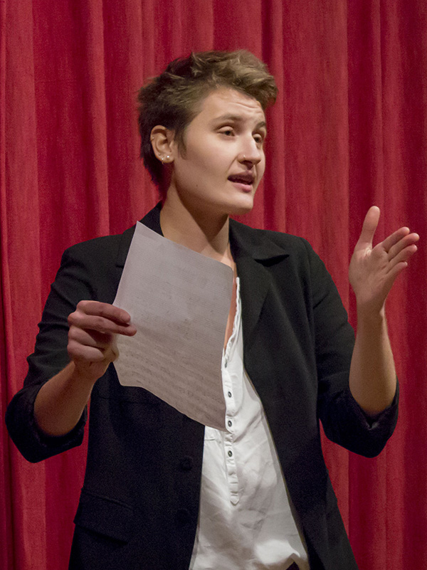 A person holding a piece of paper speaks in front of a red curtain