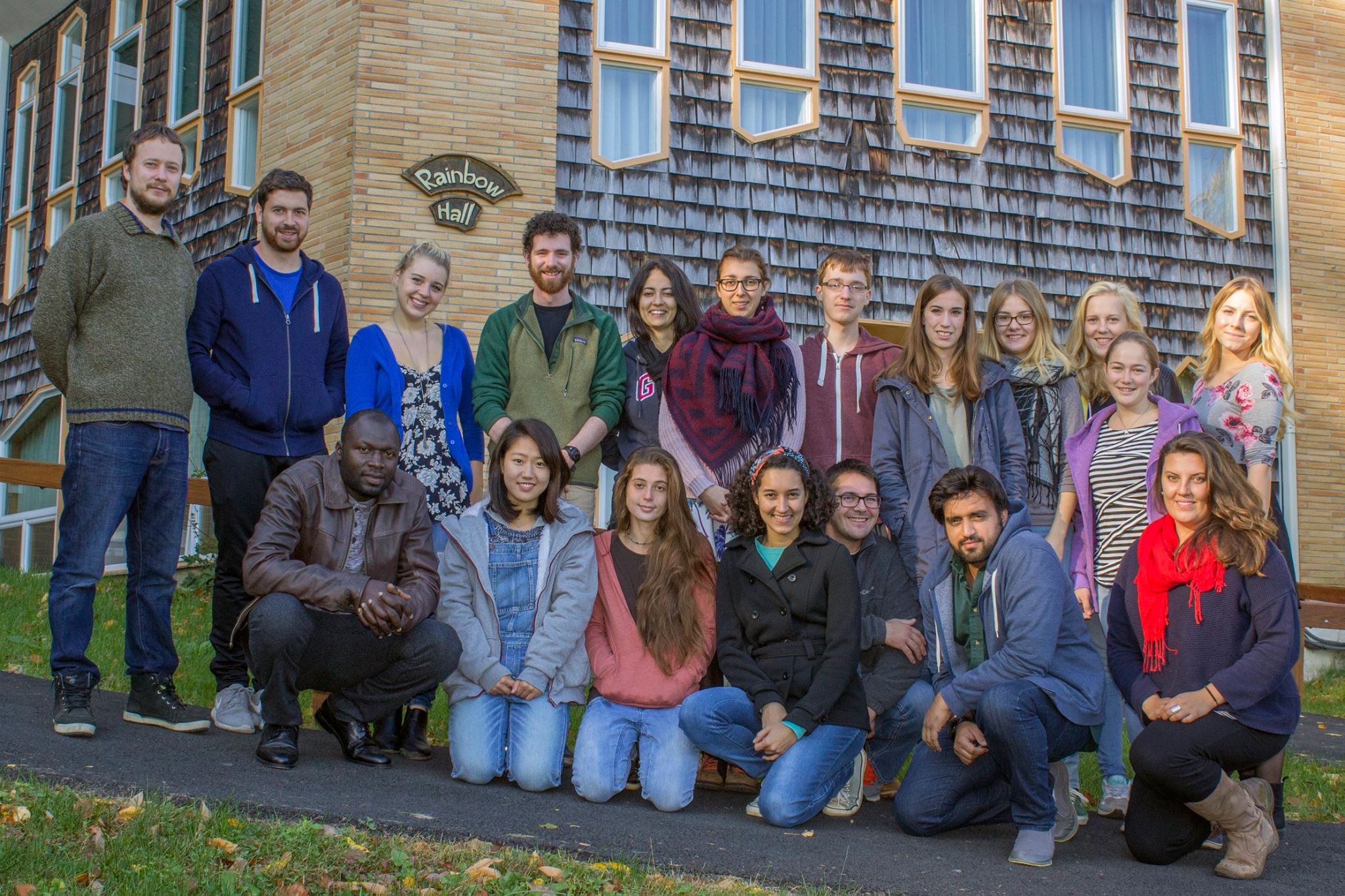 A group of students pose together outdoors in front of Rainbow Hall.