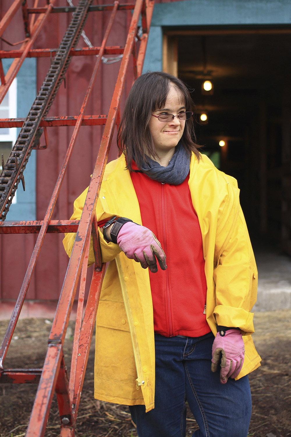 A woman in a yellow rain jacket and pink gardening gloves stands outside