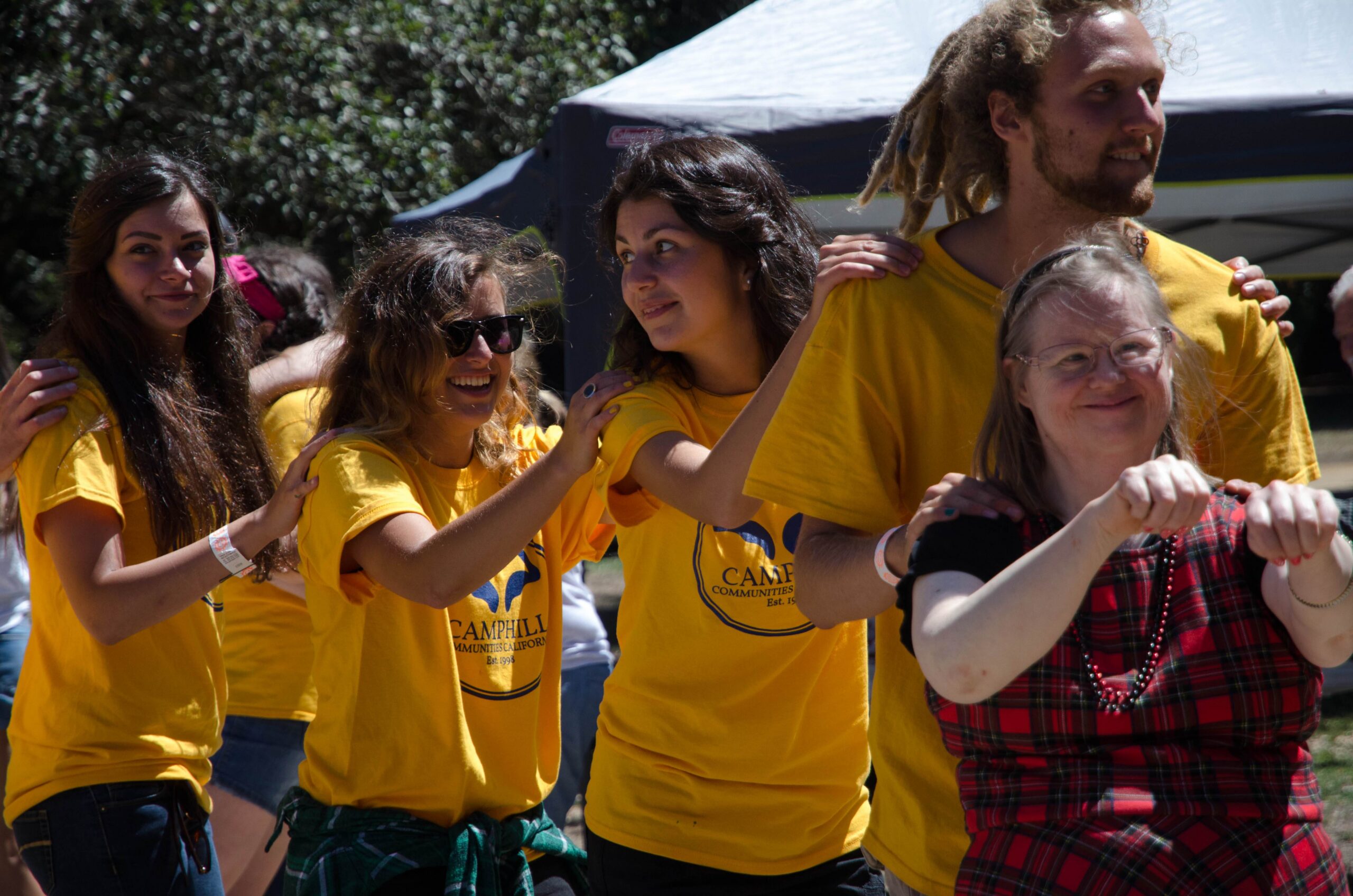 Four volunteers in yellow shirts and a Camphill resident in a red dress dance together in a line