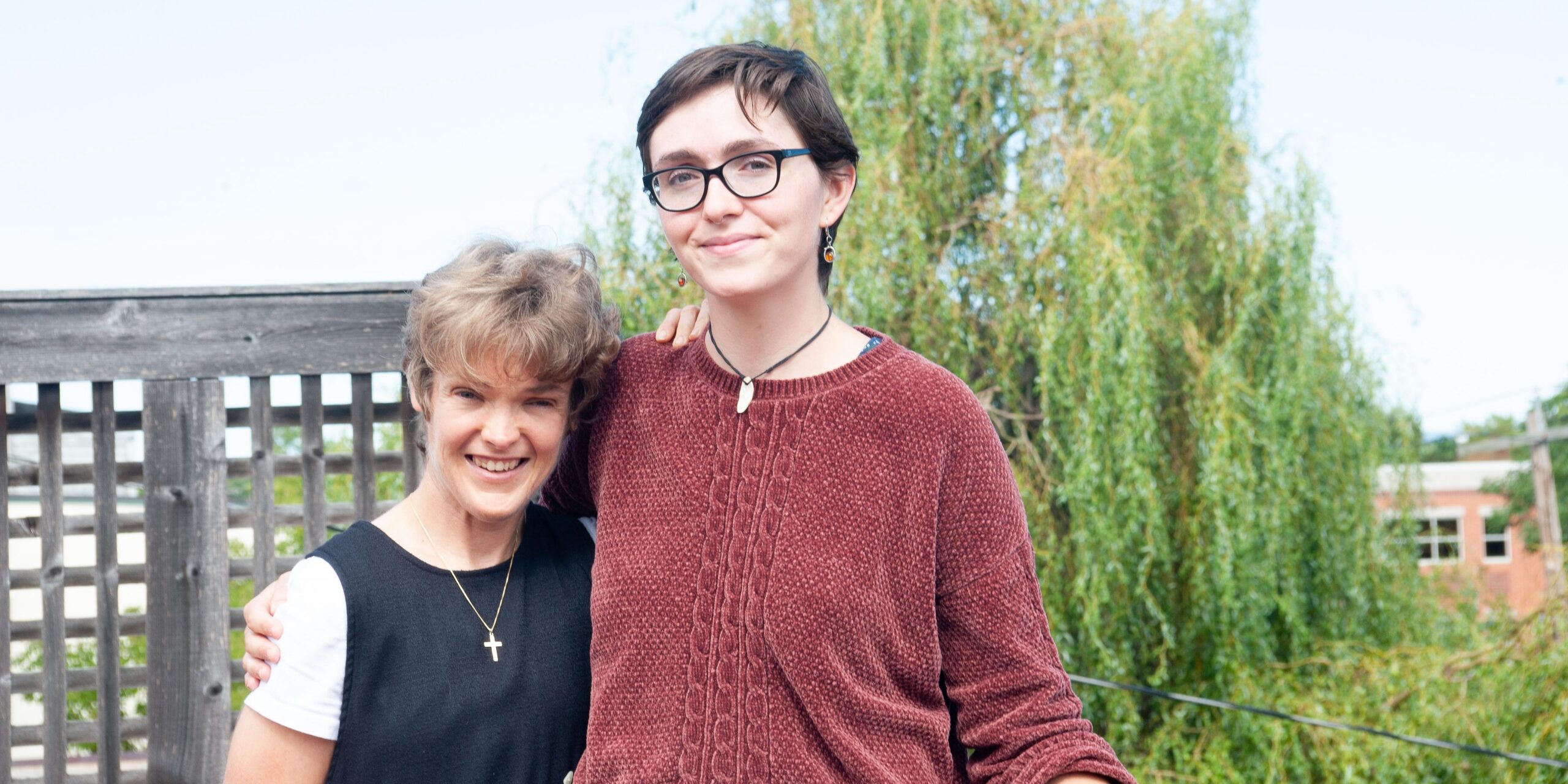 Two people hugging each other and smiling for the camera in front of a tree
